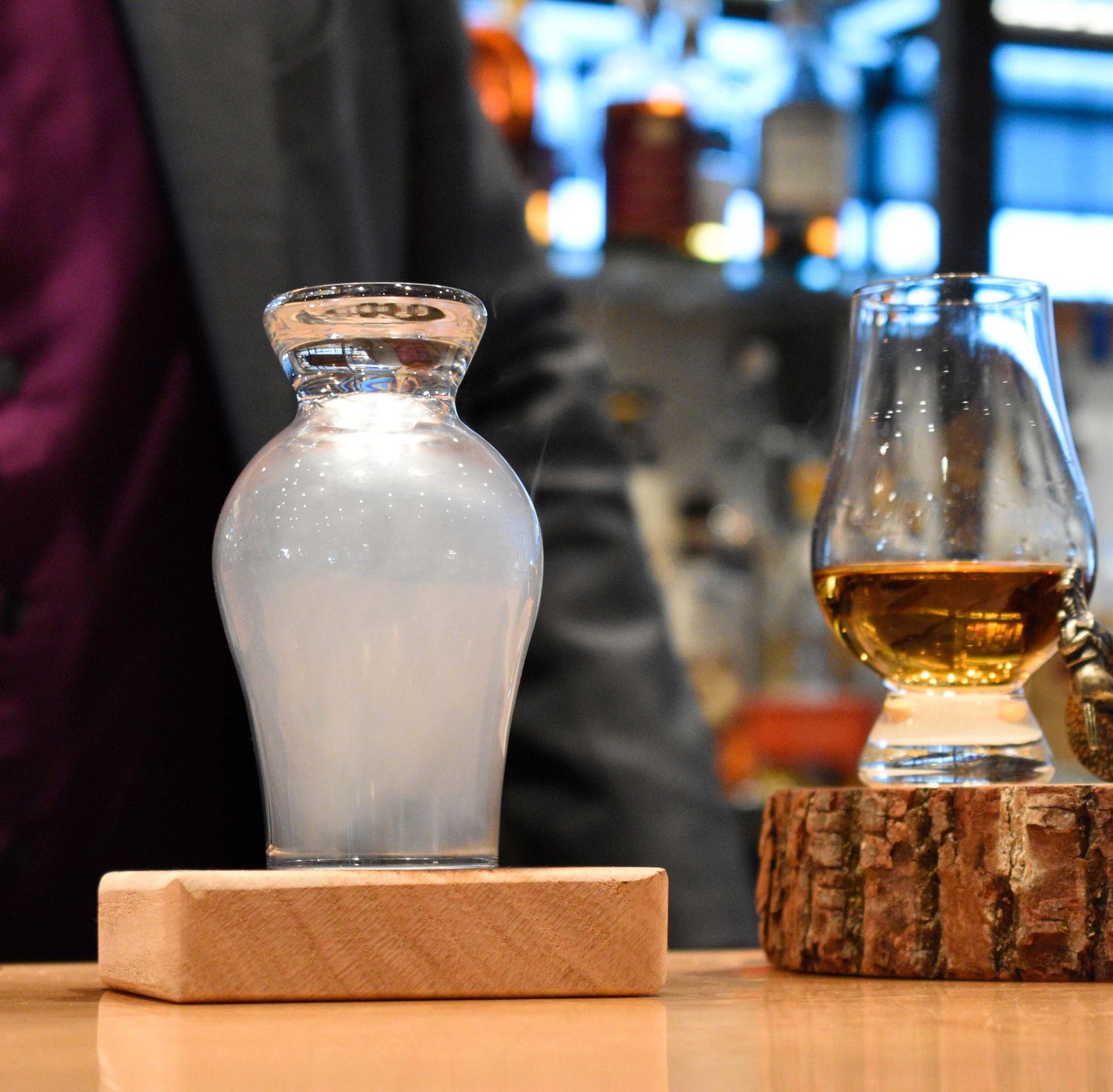 Frosted glass vessel beside a Glencairn whisky glass on a wooden log coaster.