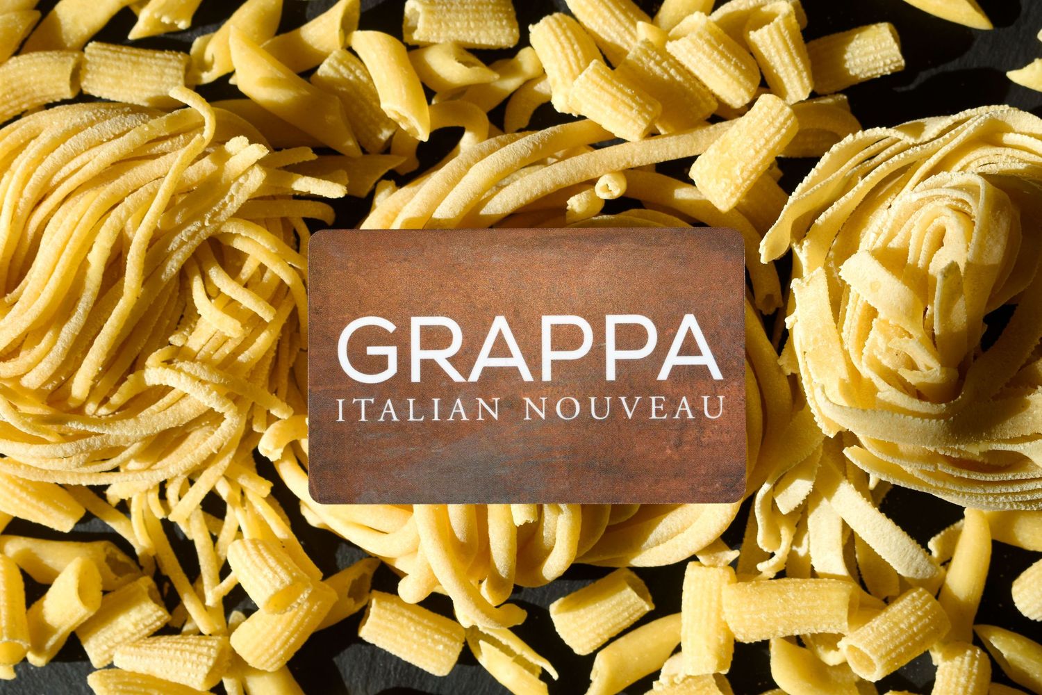 Grappa Italian Nouveau restaurant card surrounded by assorted uncooked pasta varieties.