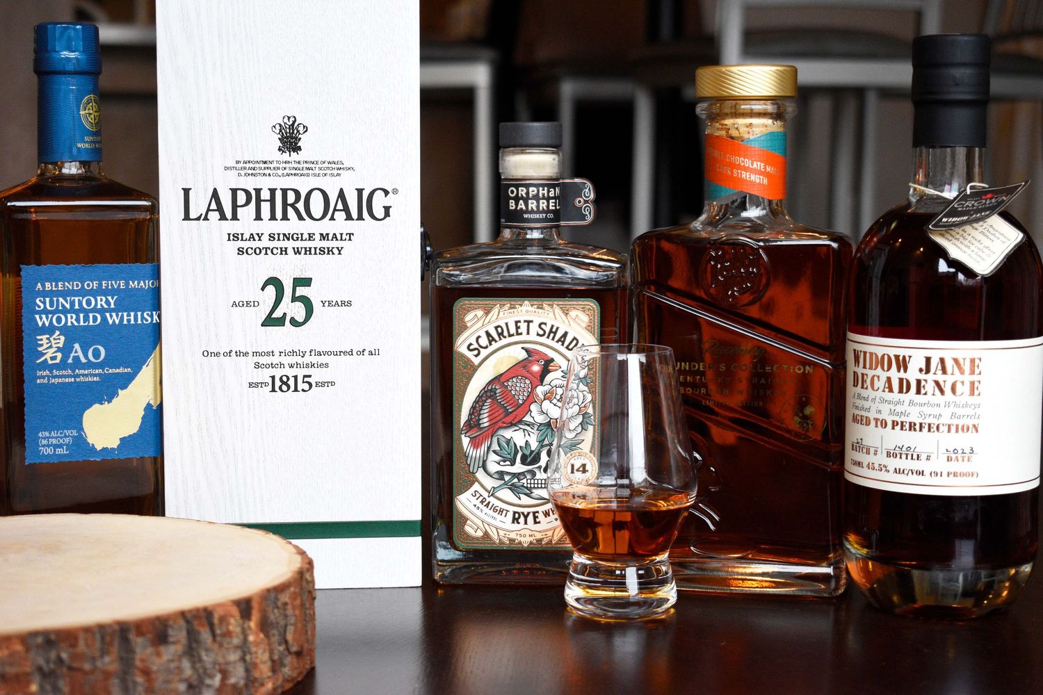 Premium whiskey bottles including Laphroaig 25 Year Scotch and Scarlet Shade Rye arranged with a crystal tasting glass.