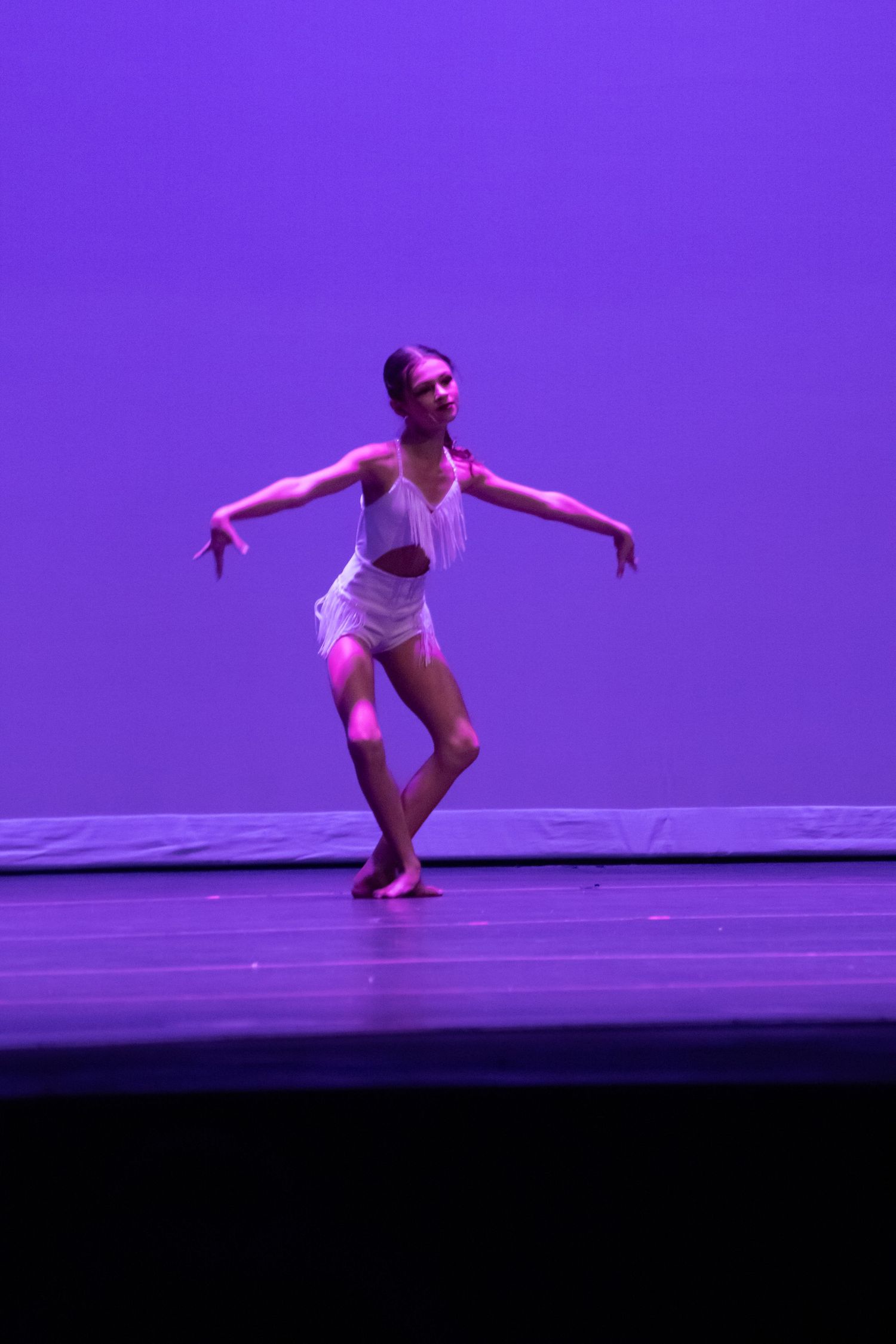 A dancer in a white outfit performs on a purple-lit stage.