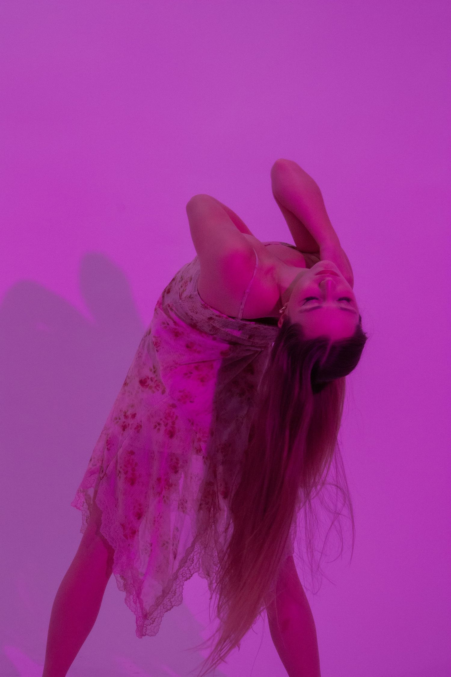 Dancer in floral dress bending back dramatically in purple-lit studio.