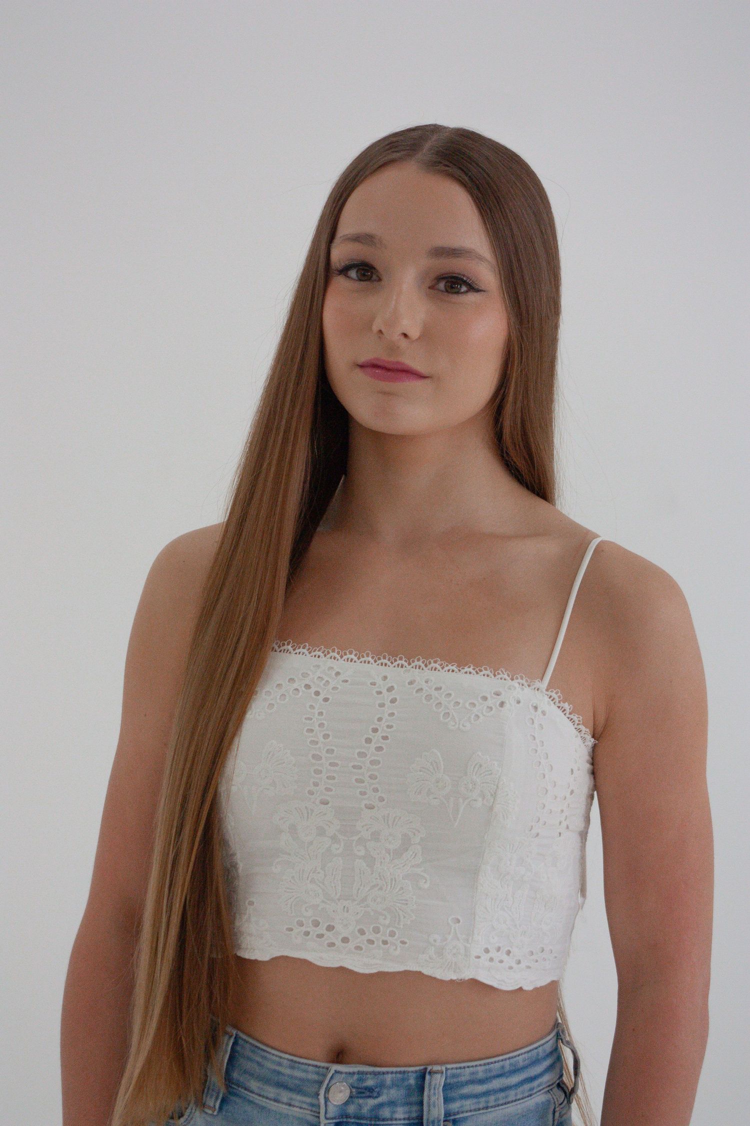 Young woman with long straight hair wearing white lace crop top and jeans.