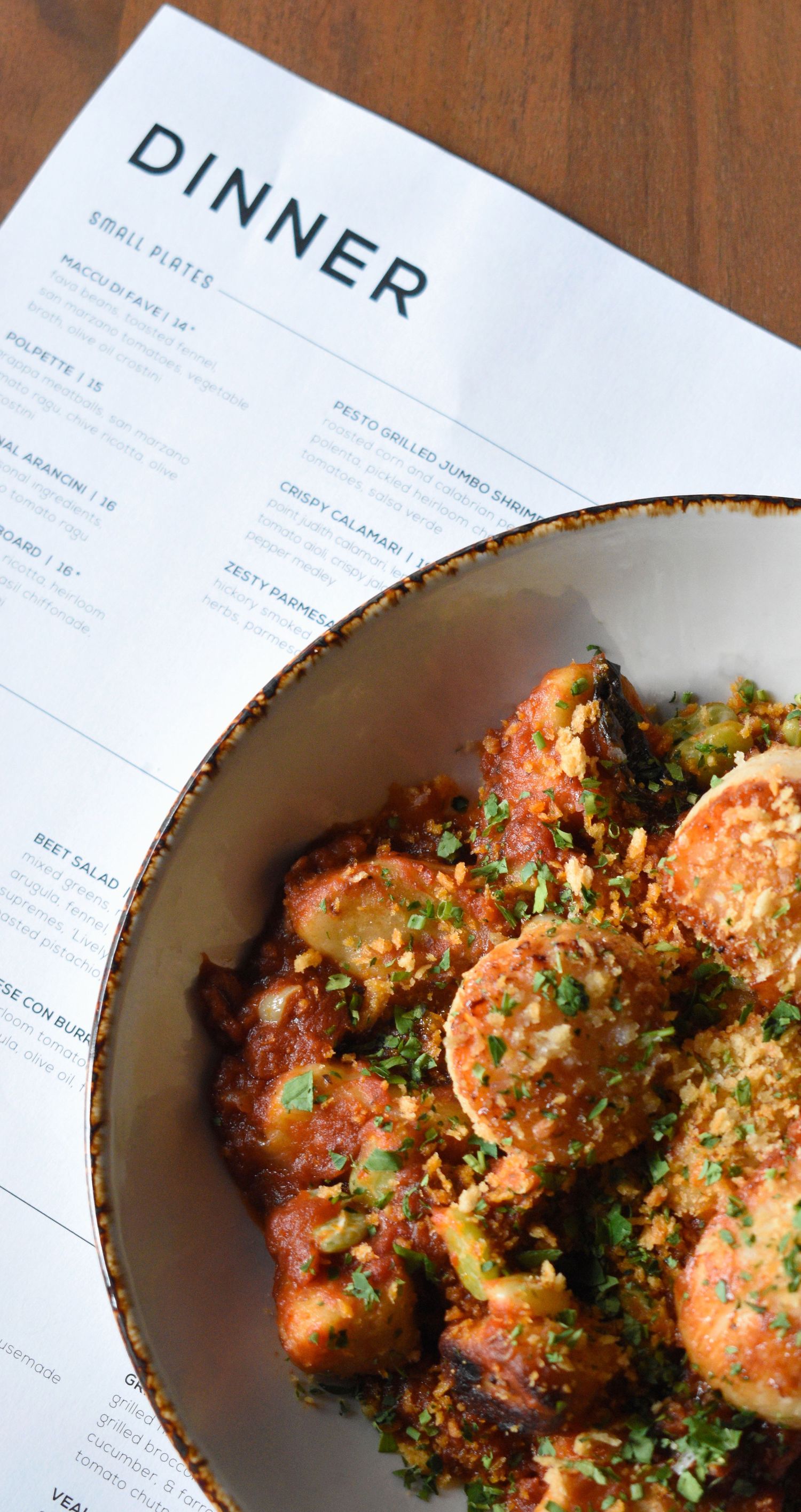 Bowl of polpette Italian meatballs in tomato sauce with breadcrumbs beside a dinner menu.