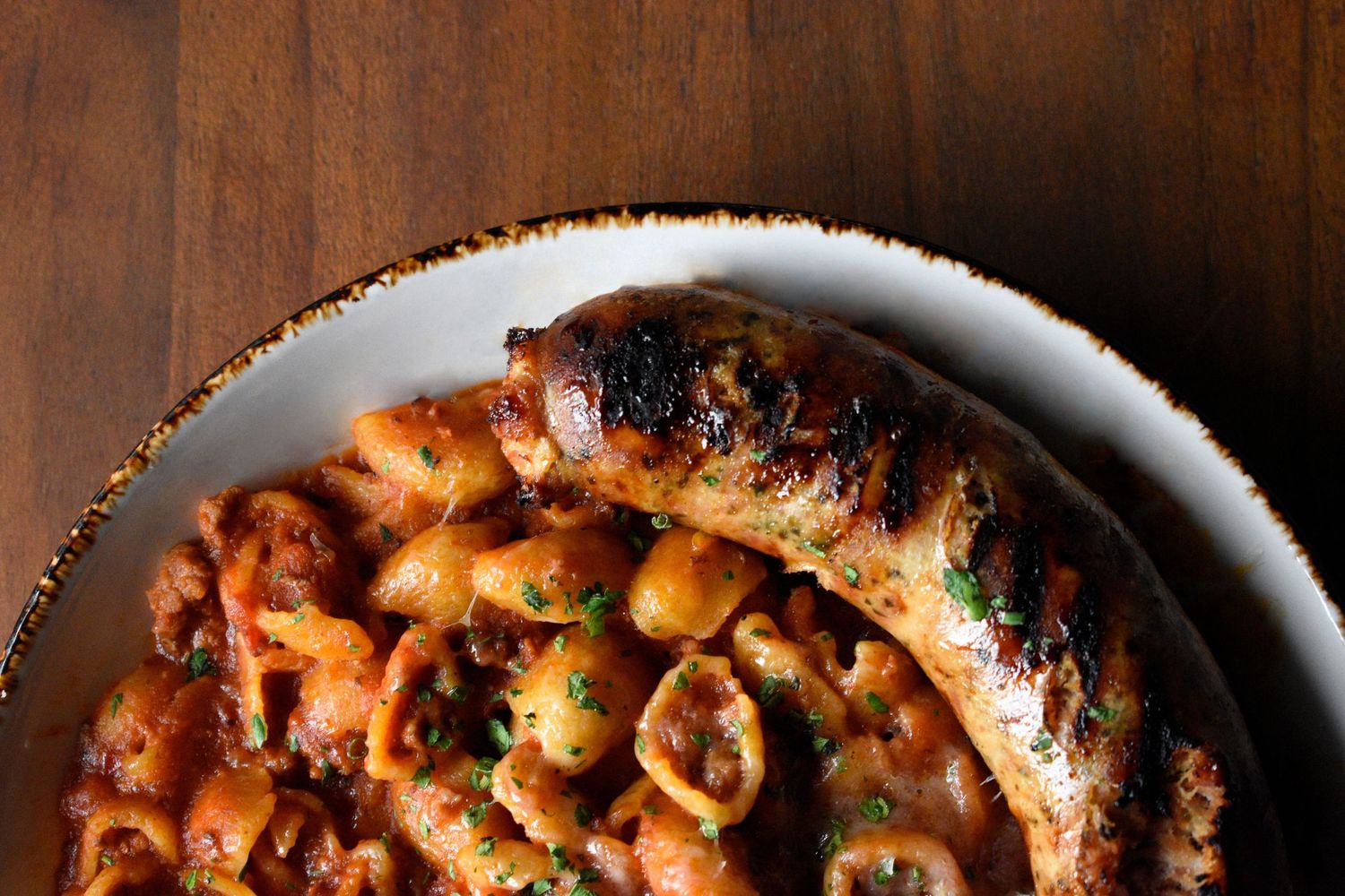 Pasta e fagioli with sausage in a rustic ceramic bowl on a warm wooden surface.