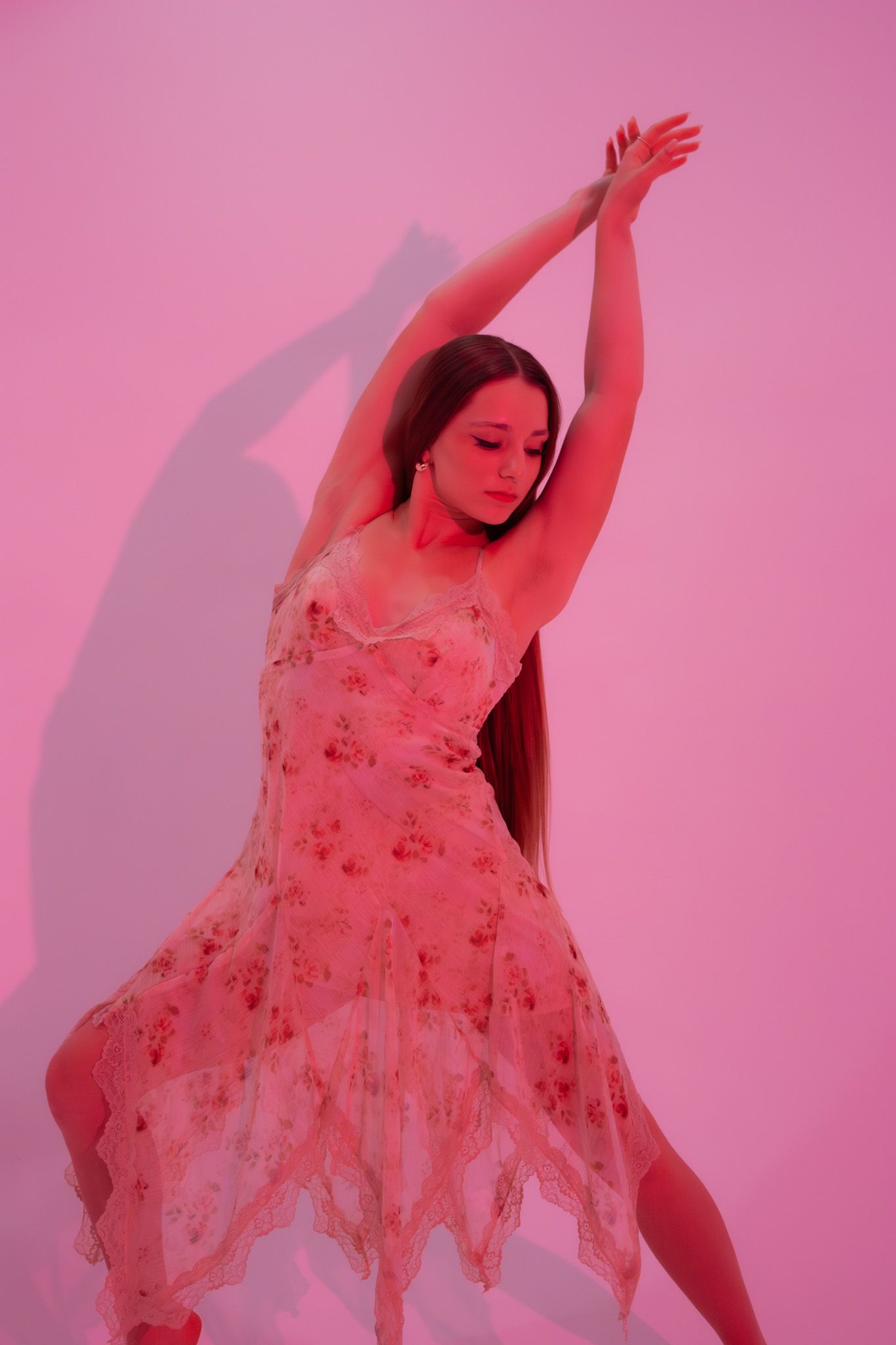 Dancer in floral dress with arms raised performing in pink-lit studio.