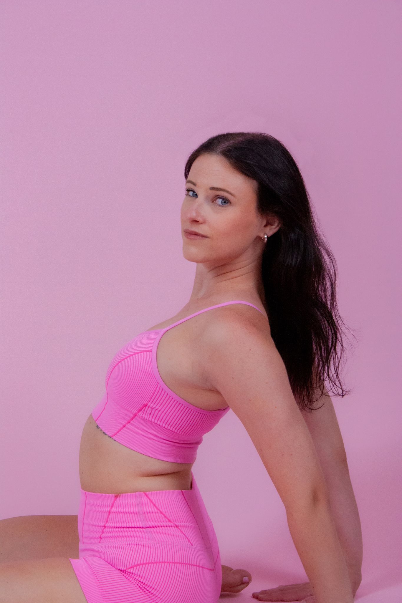 Woman in pink crop top and shorts poses against pink background, showcasing matching activewear set.