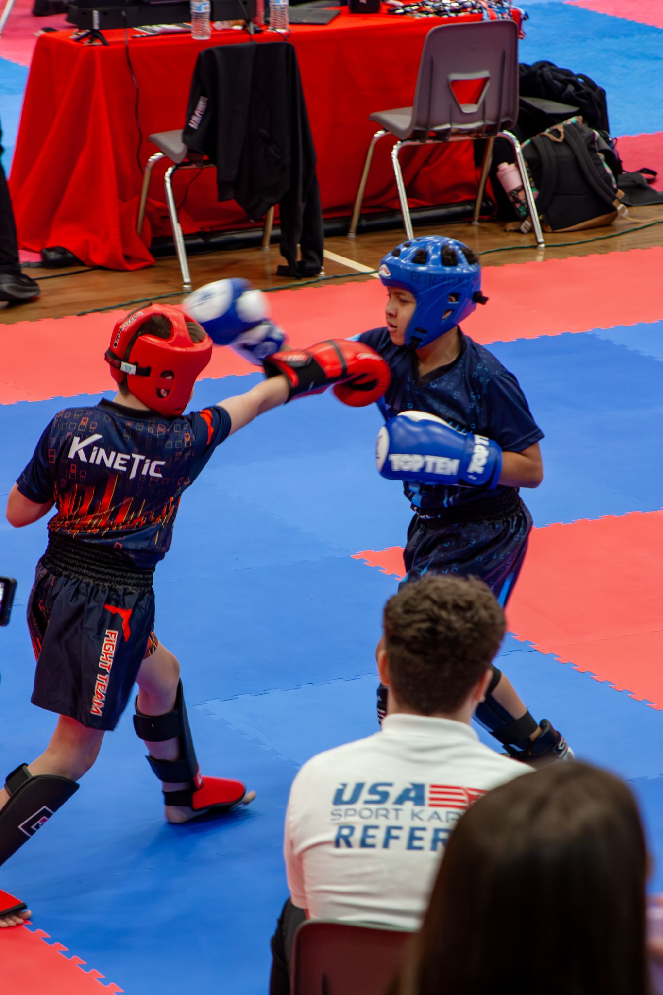 Two young karate fighters spar in full protective gear at a USA Sport Karate tournament.