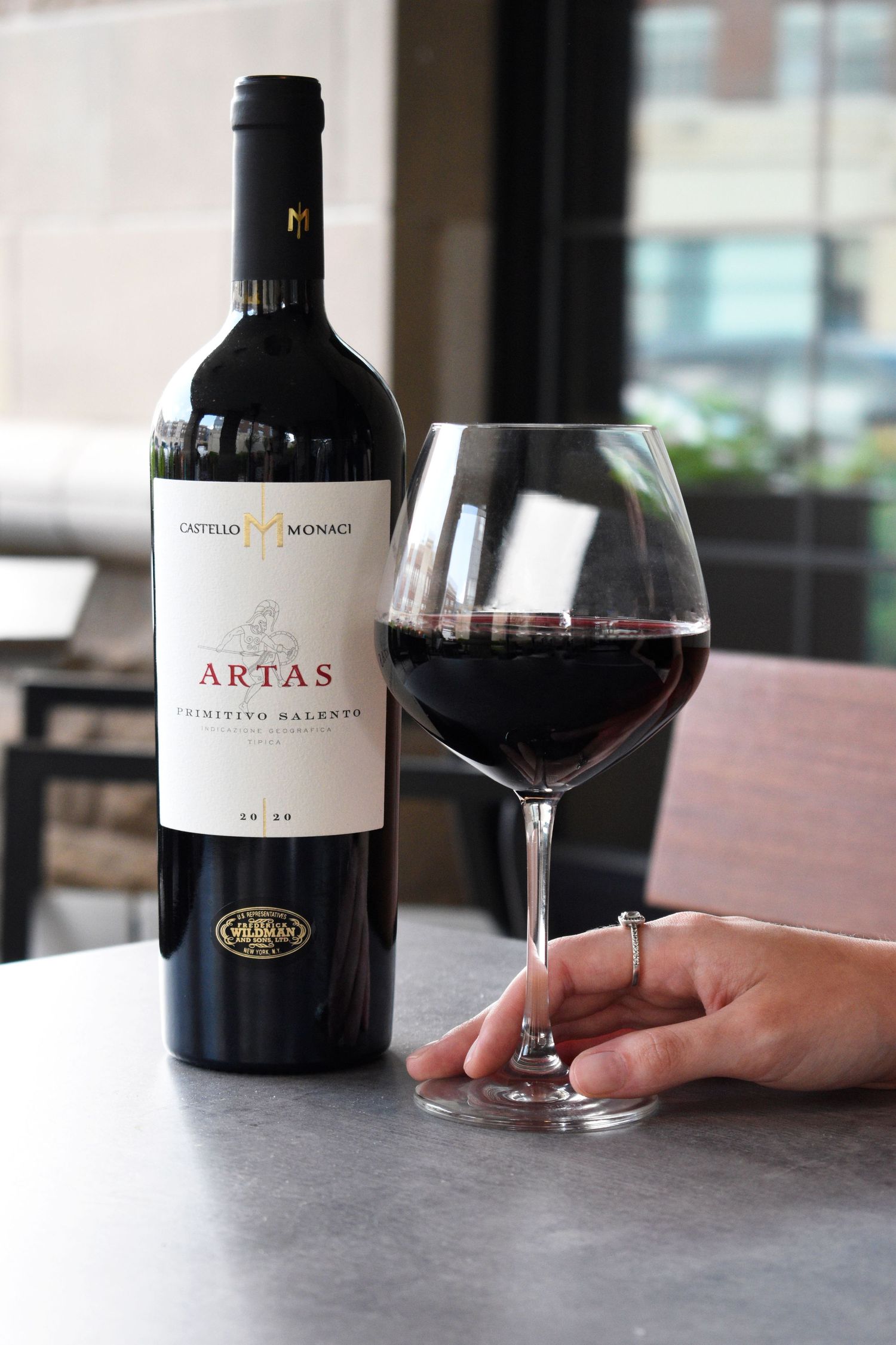 Bottle of Castello Monaci Artas Primitivo Salento red wine with a poured glass.