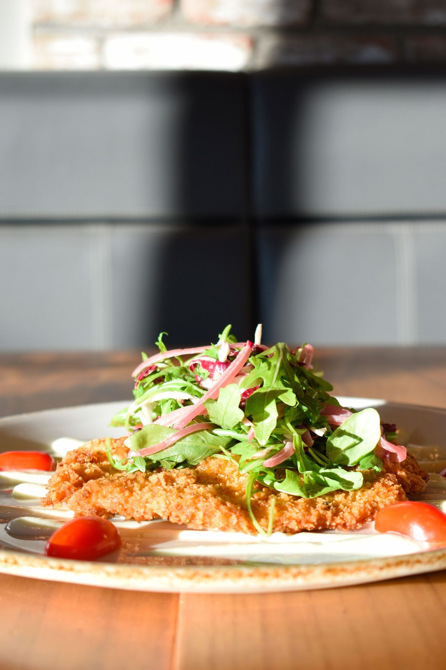 Crispy breaded chicken cutlet topped with fresh arugula salad and cherry tomatoes on a plate.