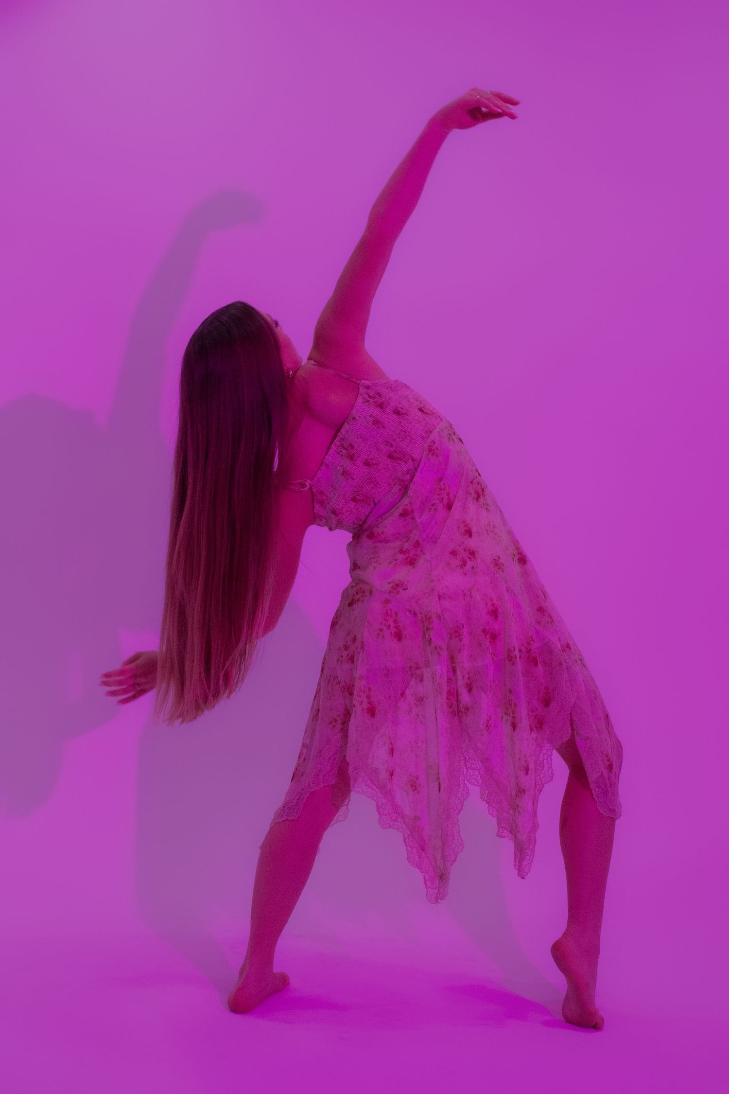 Dancer in floral dress performing a graceful side bend under vibrant purple studio lighting.