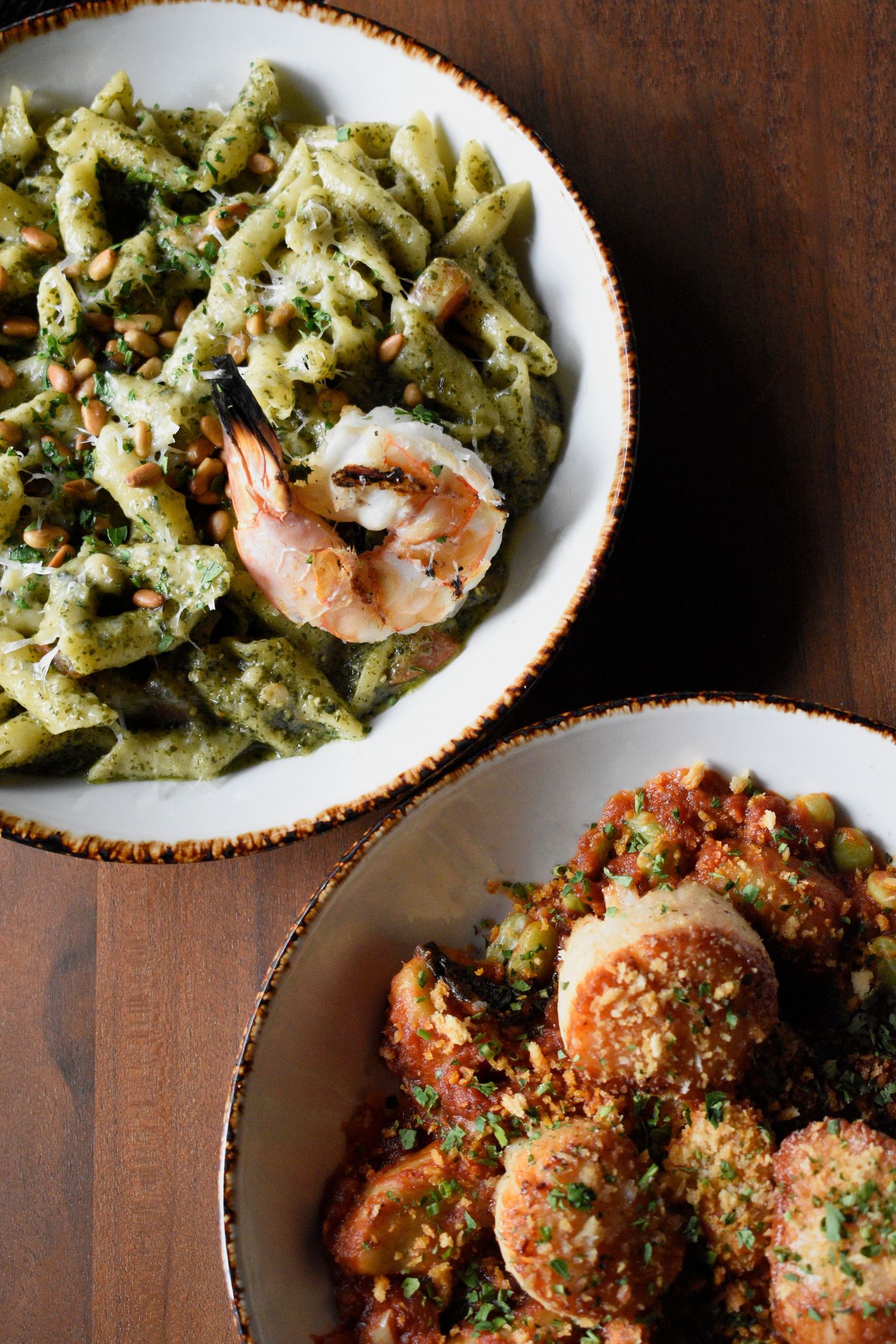 Overhead view of pesto shrimp penne pasta and baked scallops in rustic bowls.
