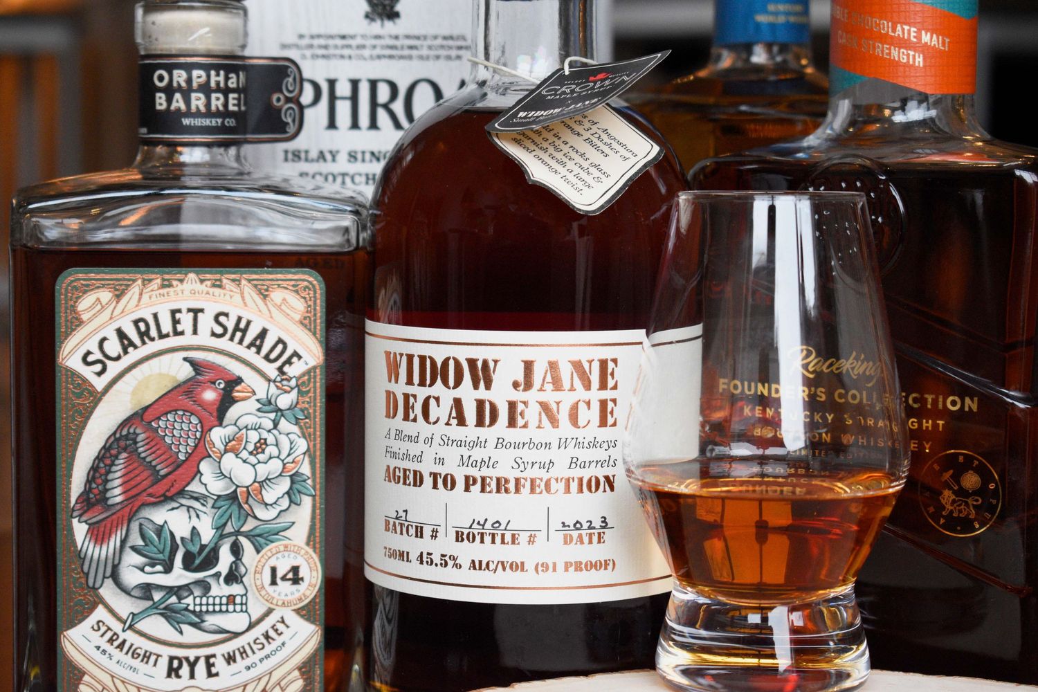 A collection of premium whiskey bottles including Widow Jane Decadence and Scarlet Shade Rye with a tasting glass.