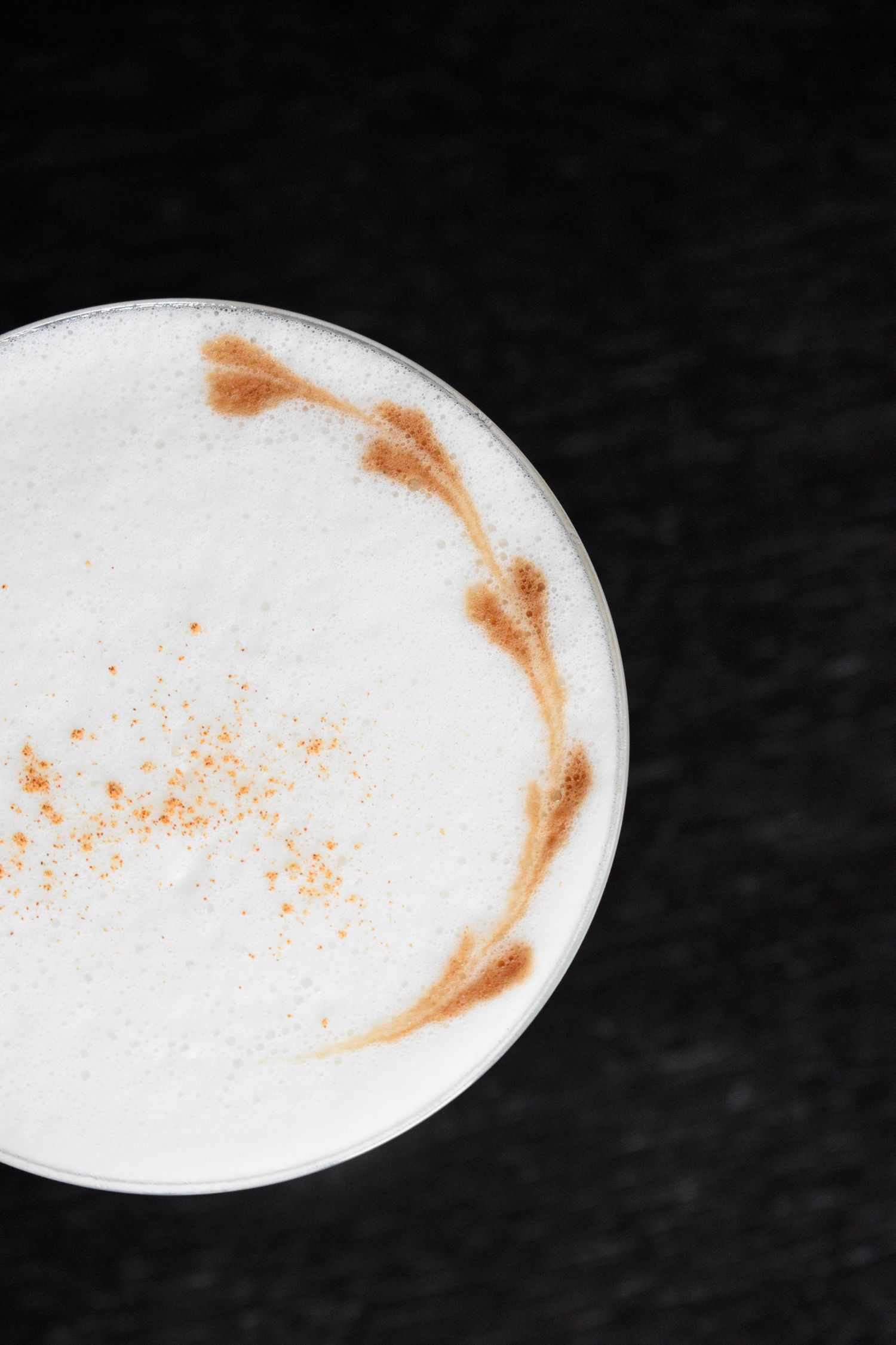 Overhead view of a creamy cappuccino with cinnamon art on white milk foam in a glass cup.