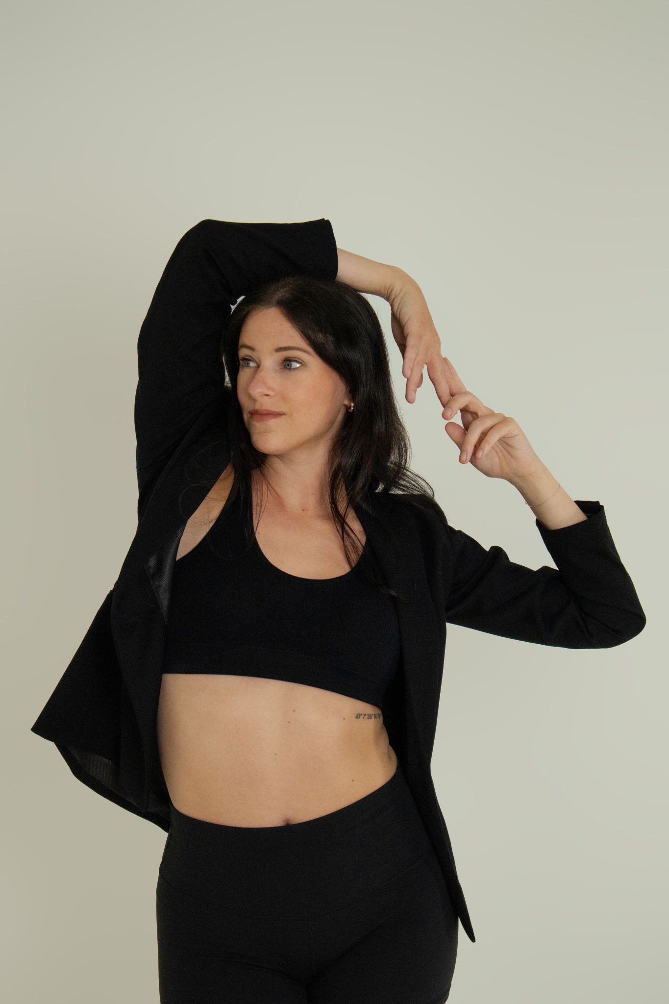 Woman in black crop top and blazer posing dynamically in studio.