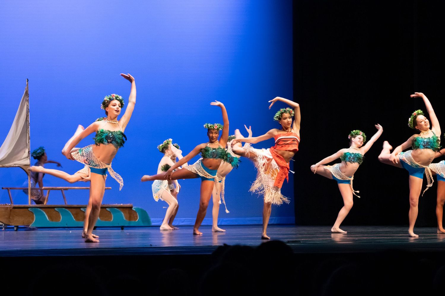Young dancers in tropical costumes perform a vibrant group routine on a bright stage.