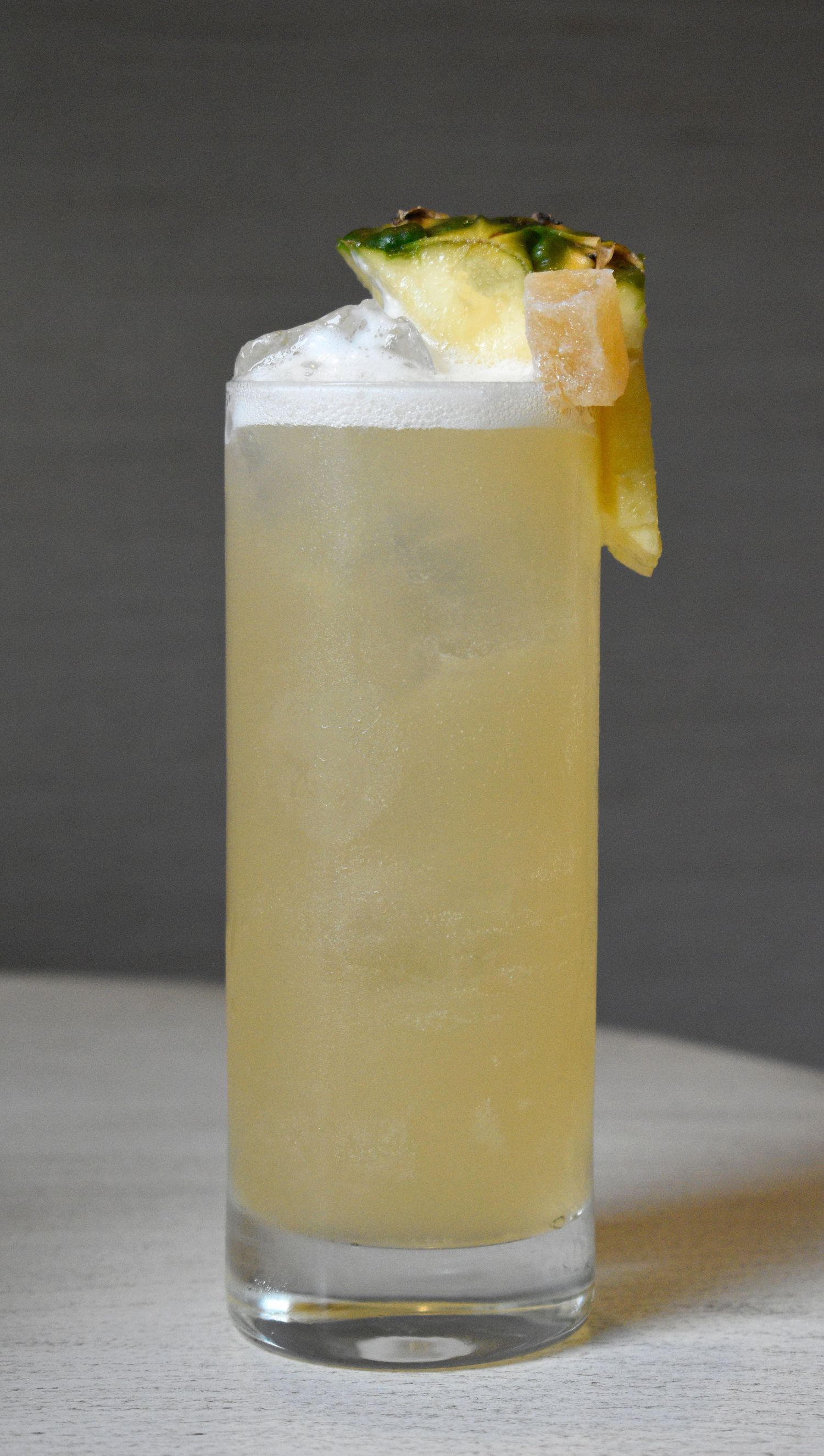 A tall pineapple cocktail in a highball glass with crushed ice, garnished with a fresh pineapple wedge.