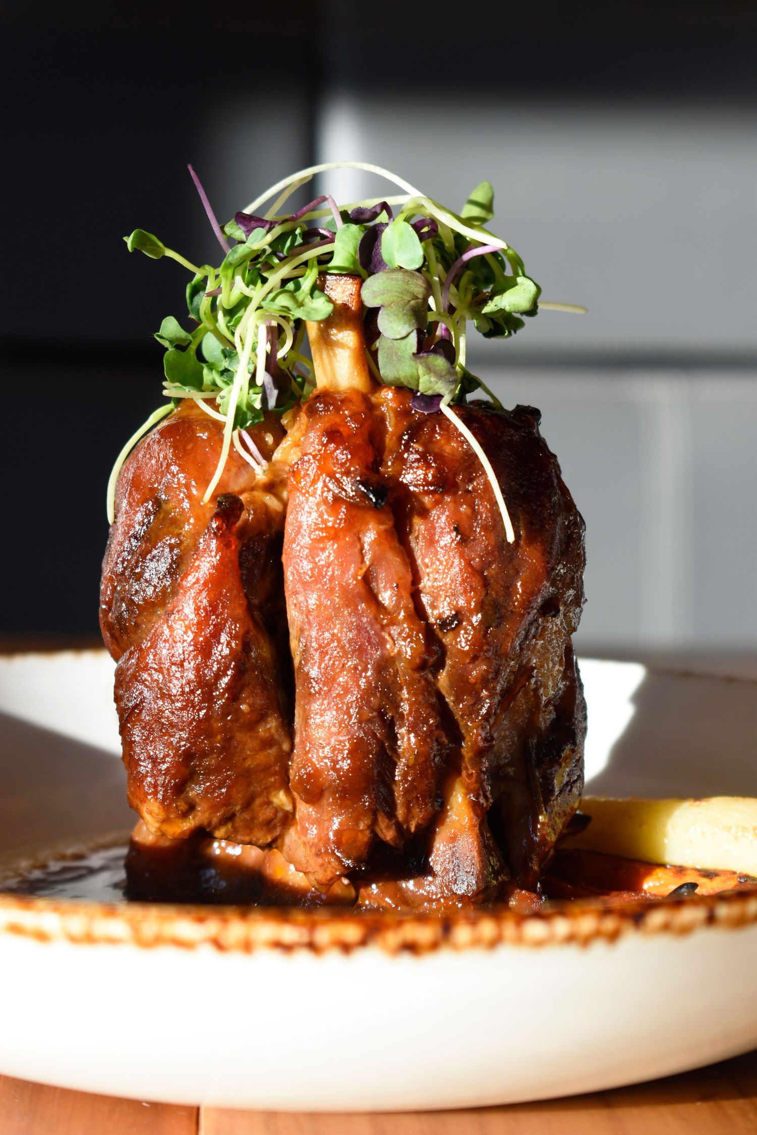 Glazed braised short rib standing upright on white plate garnished with fresh microgreens.