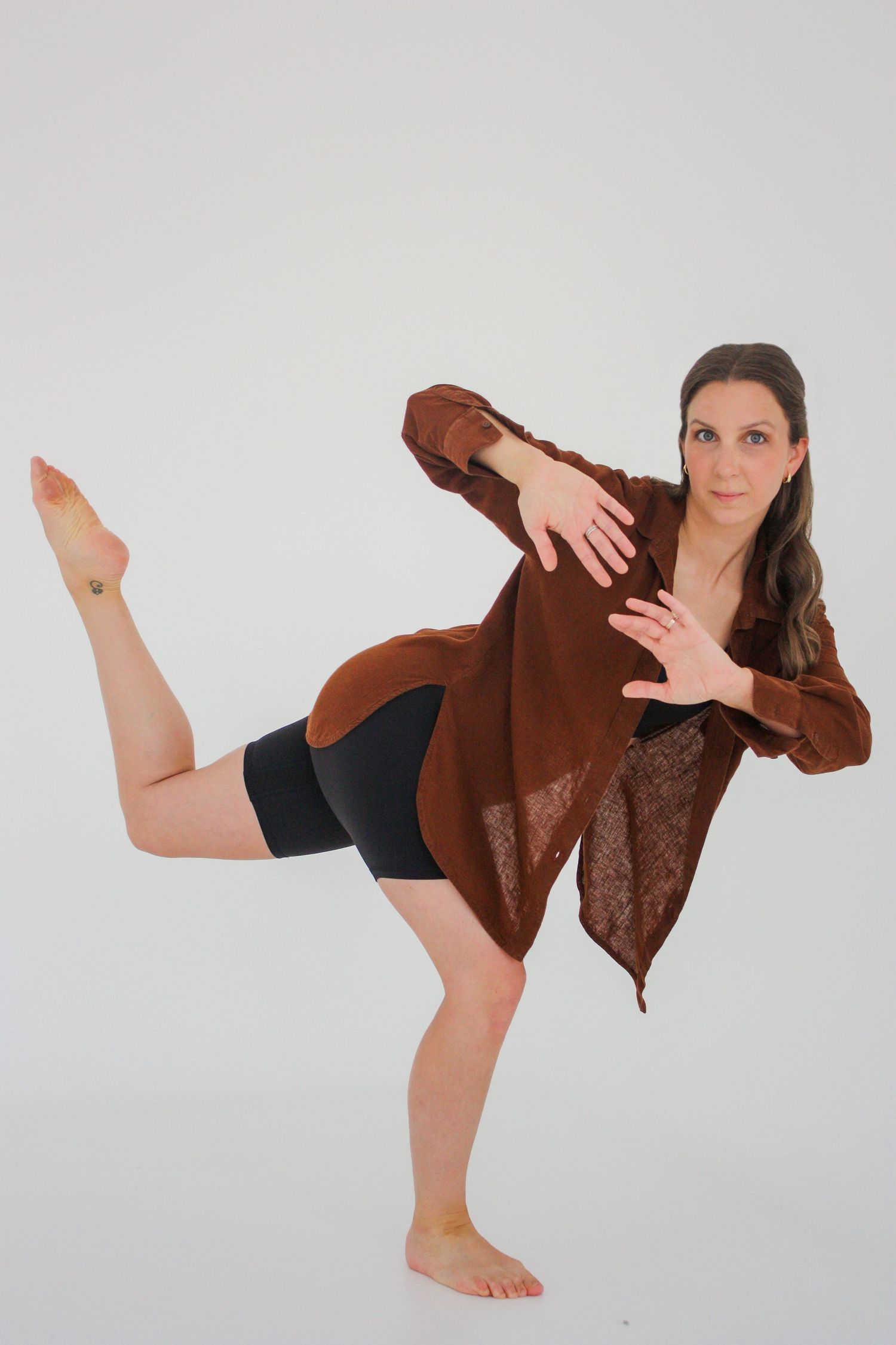 Woman in brown cardigan and black shorts balancing on one foot with leg raised in a dance pose. Branding photography Tampa, FL.