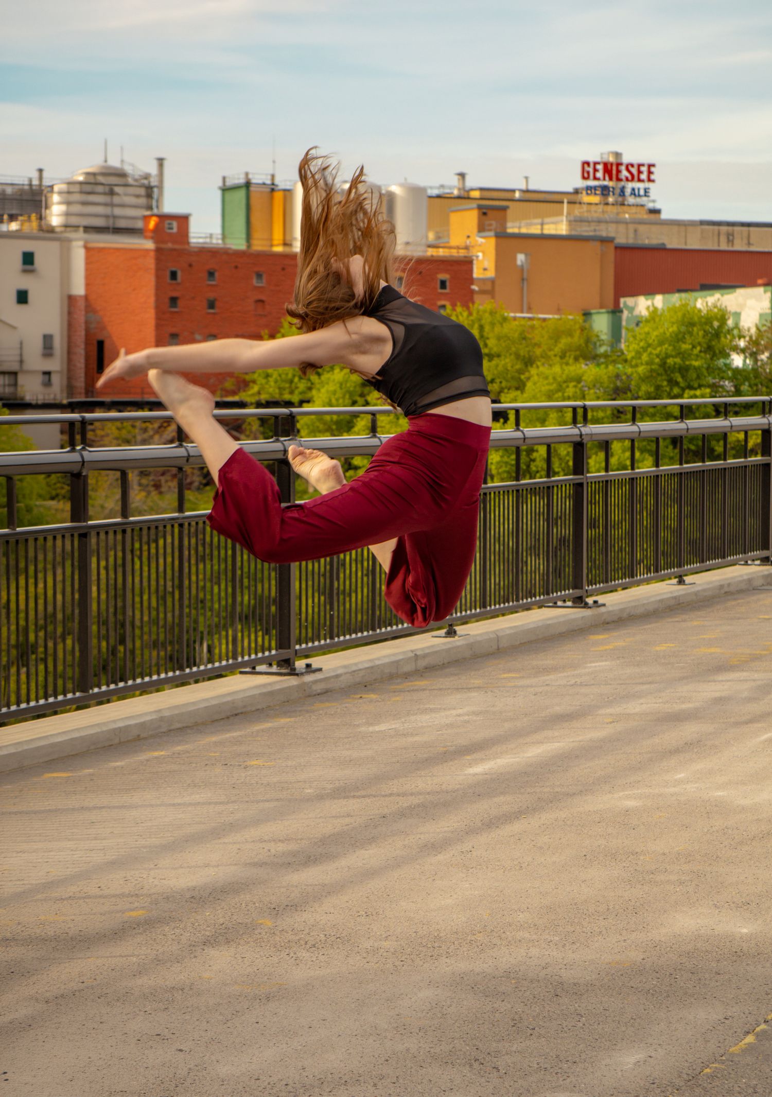 Female dancer performing high jump split leap on urban rooftop with city skyline.