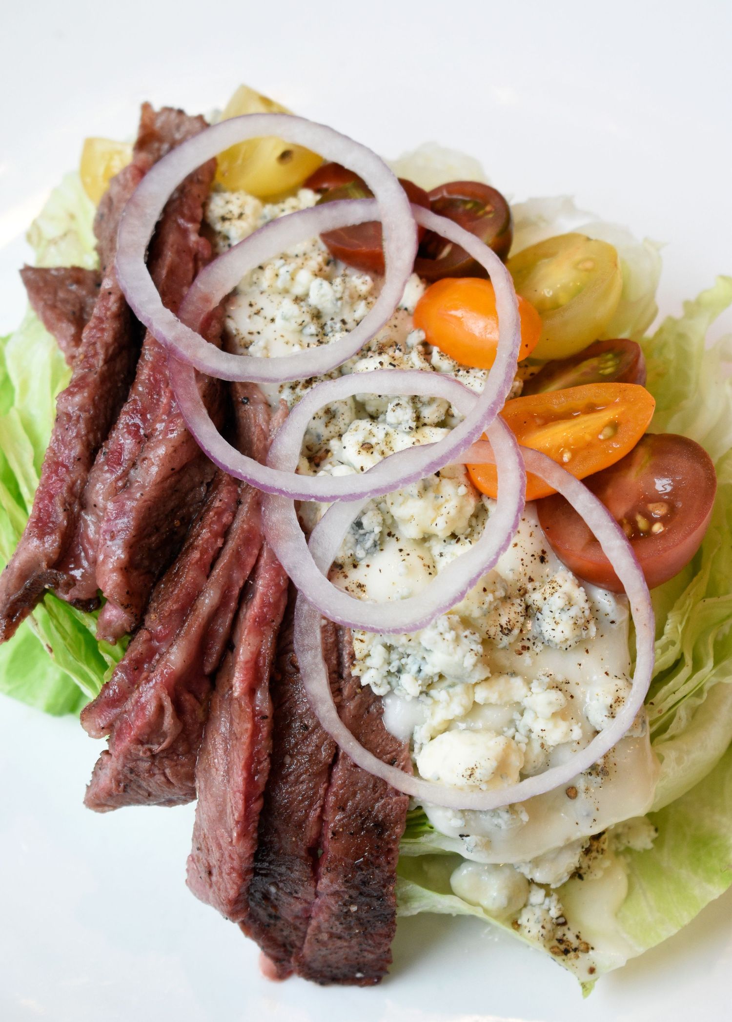 Grilled skirt steak salad with blue cheese, cherry tomatoes, and red onion rings on crisp lettuce.