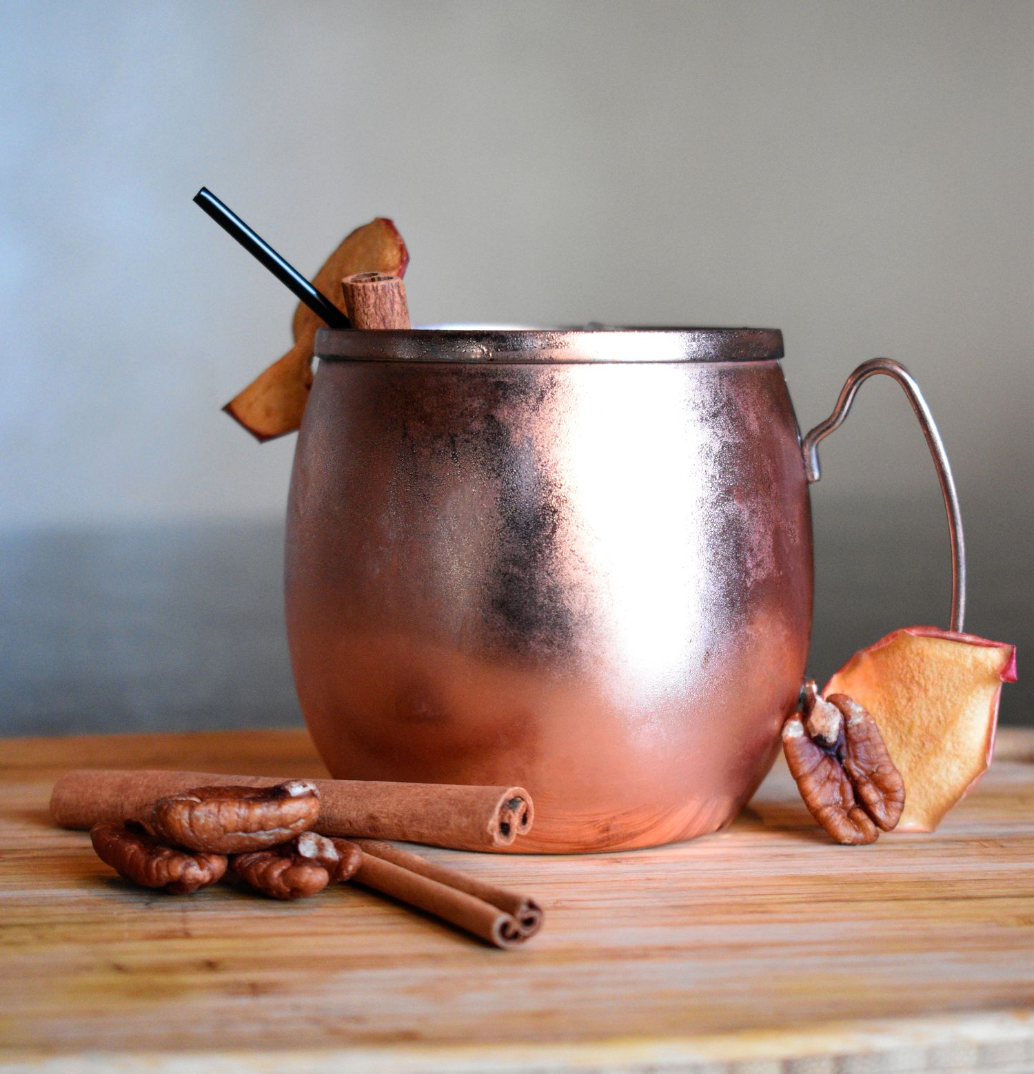 A copper Moscow mule mug garnished with cinnamon sticks and dried fruit on a rustic wooden board.