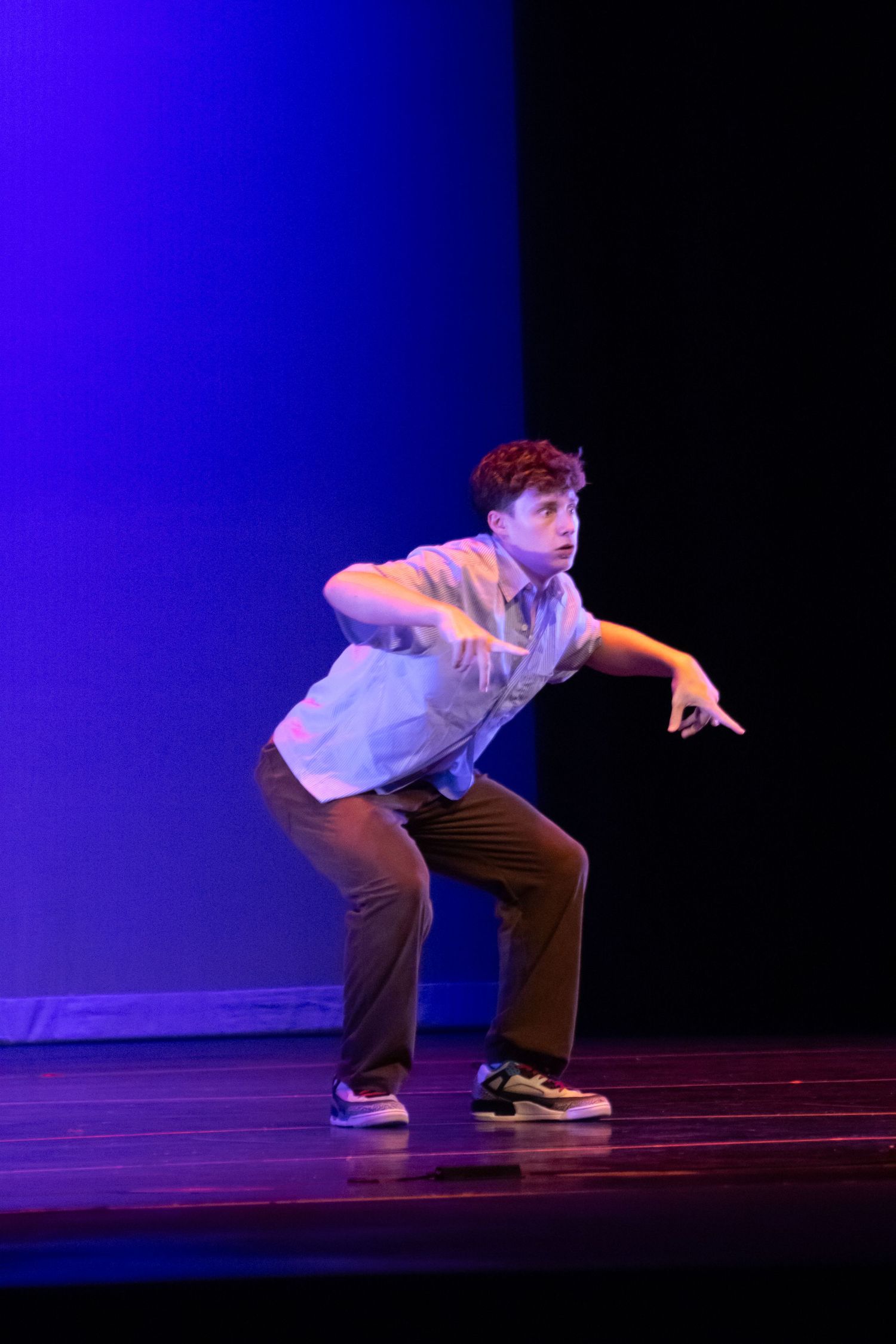 Young male dancer in casual attire performs a hip-hop routine on a blue-lit stage.