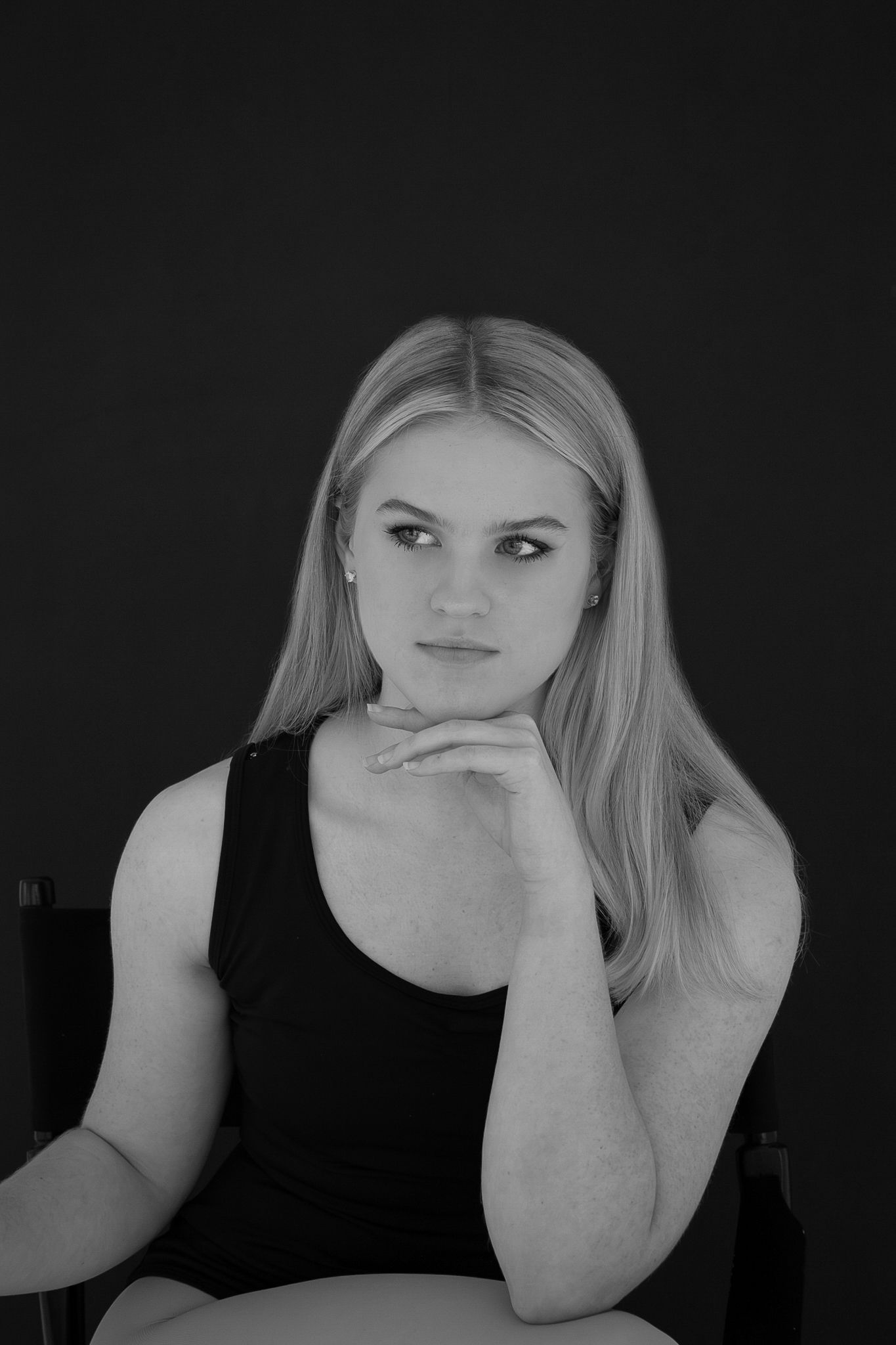 Black and white portrait of blonde dancer in black tank top resting chin on hands.
