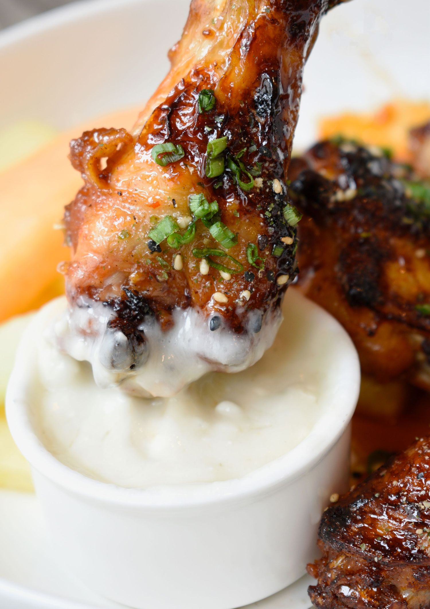 Glazed chicken wings with sesame seeds and scallions being dipped into creamy white sauce.