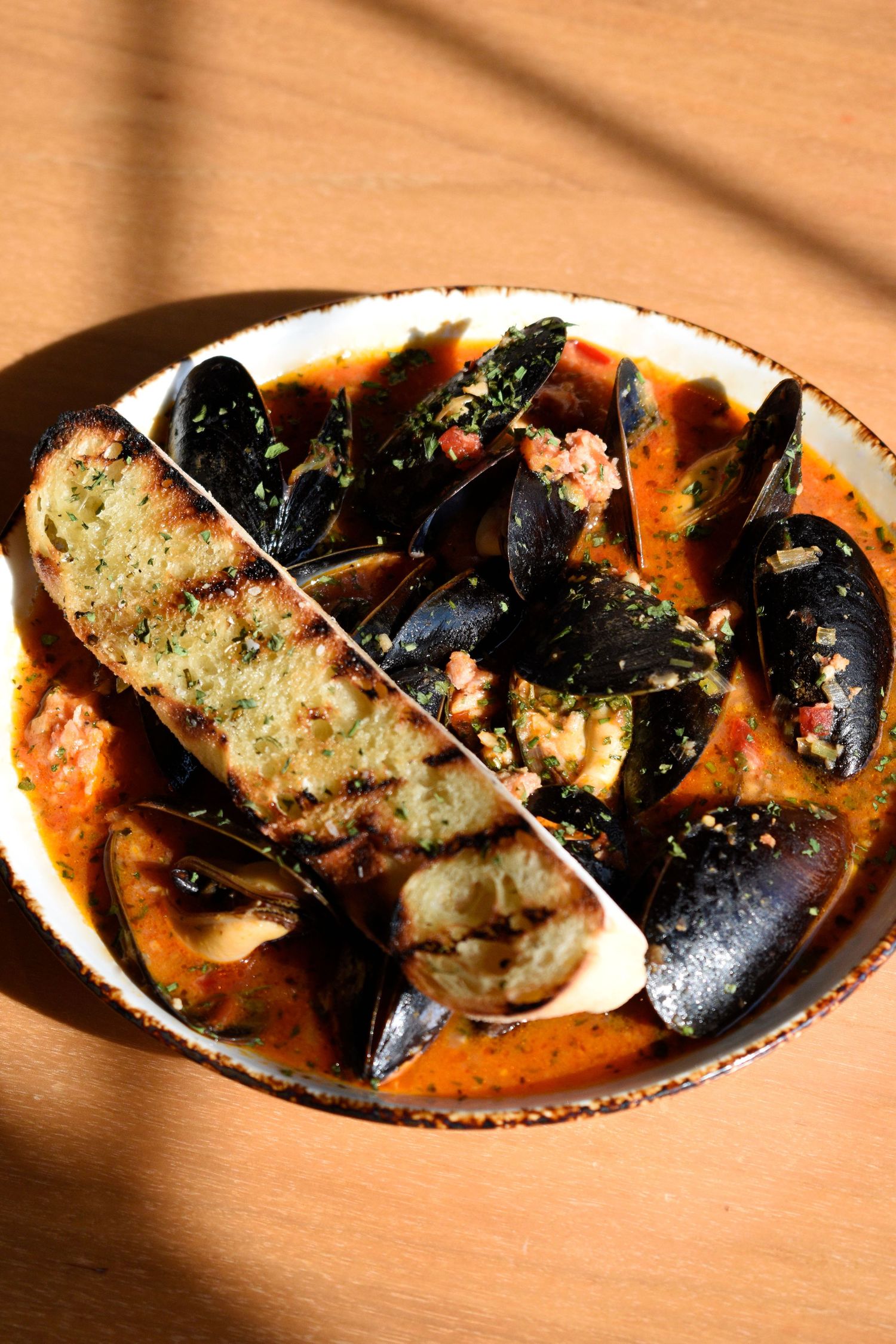Steamed black mussels in spicy tomato broth topped with herbs and served with grilled garlic bread.