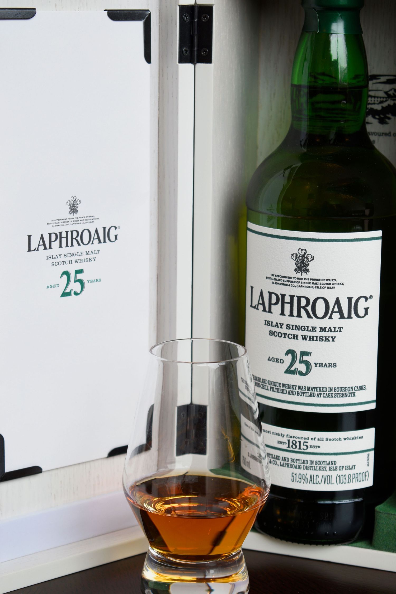 Laphroaig 25 Year Islay Single Malt Scotch Whisky bottle with Glencairn glass beside its white presentation case.