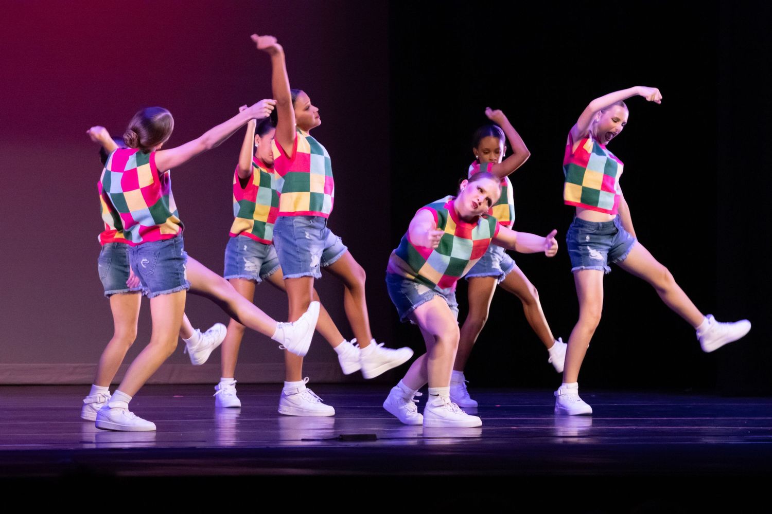Five dancers in colorful checkered tops and denim shorts perform an upbeat routine.