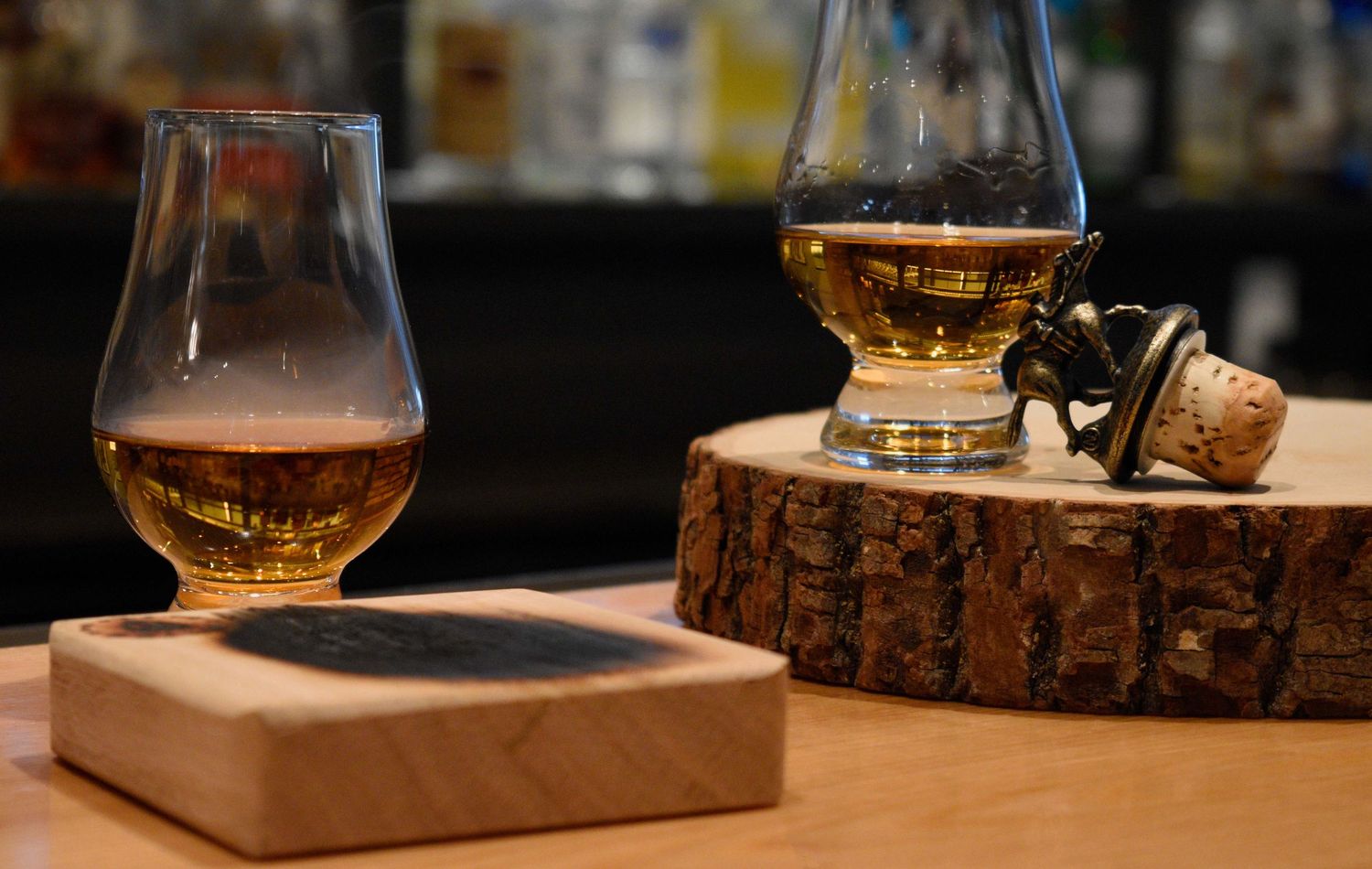 Two Glencairn whisky glasses on wooden coasters with a cork stopper at a bar.