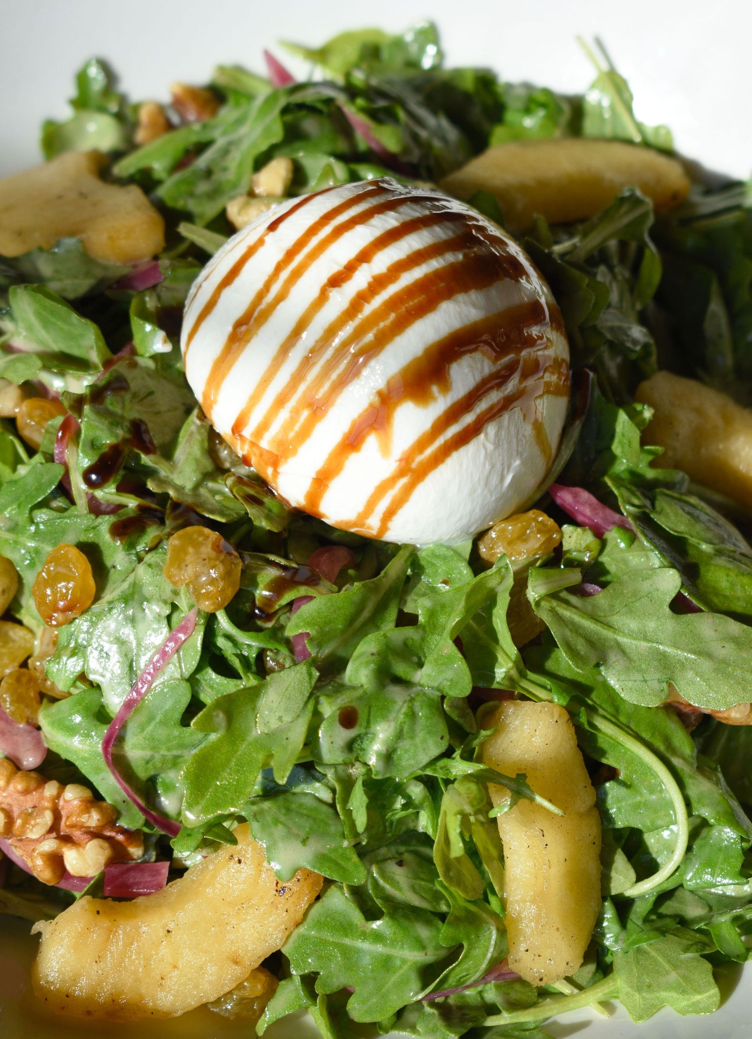 Close-up of burrata cheese with balsamic drizzle on a fresh arugula and pear salad.