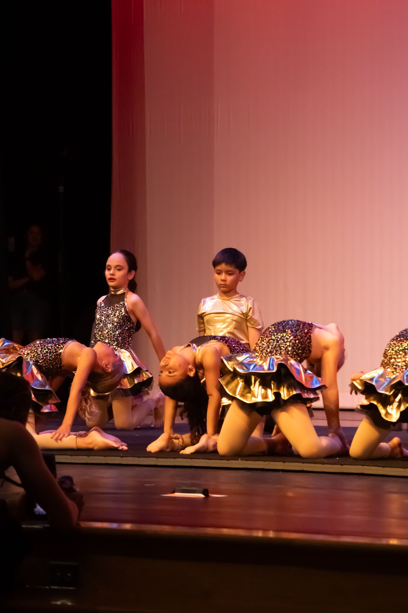 Young dancers in leopard print costumes perform a floor routine on a warmly lit theater stage.
