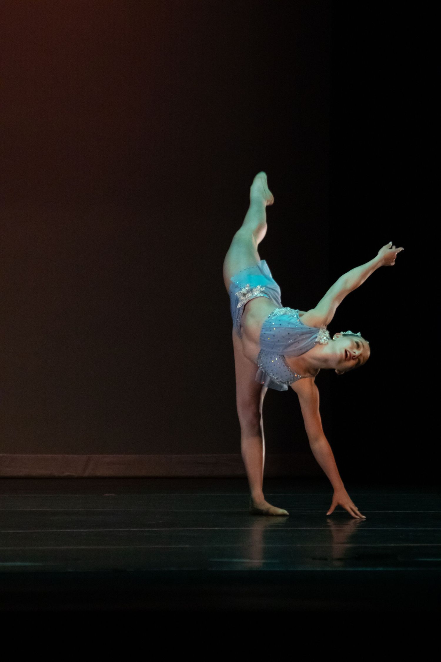 A ballet dancer executes a stunning one-handed cartwheel in a blue costume against a dark stage.