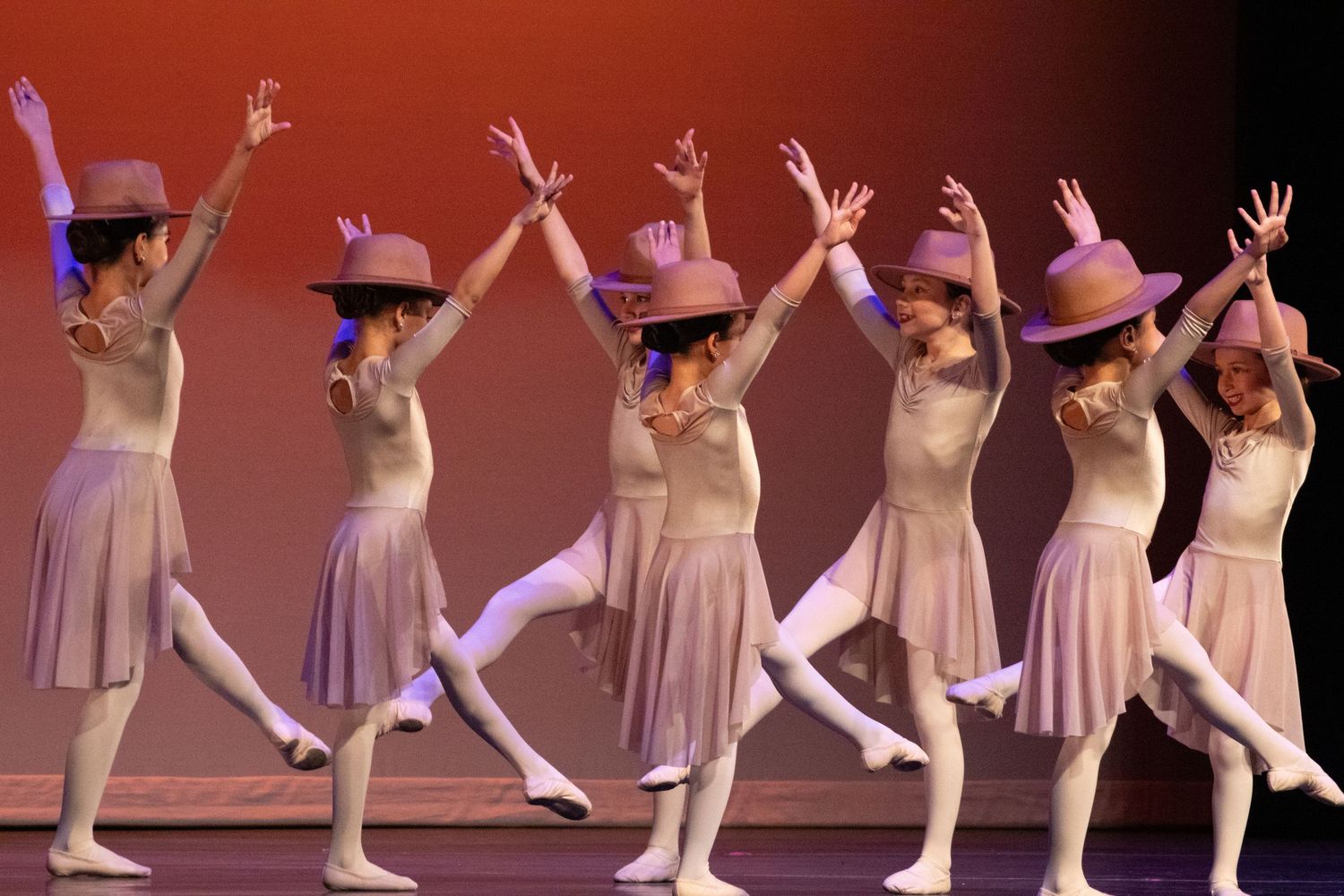 Young dancers in white dresses and pink hats perform a synchronized ballet routine.