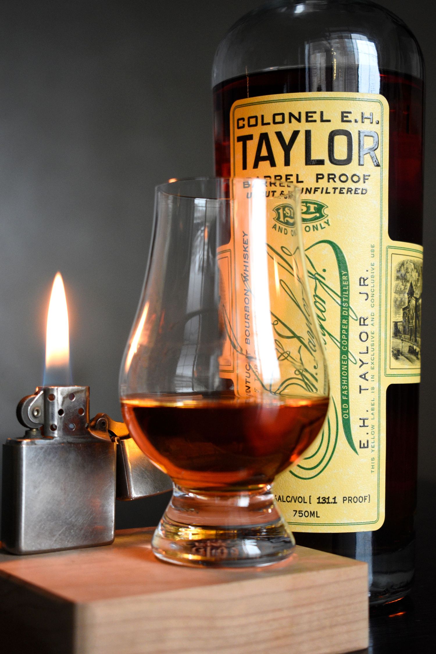 Colonel E.H. Taylor Barrel Proof bourbon bottle with Glencairn glass and lit Zippo lighter.