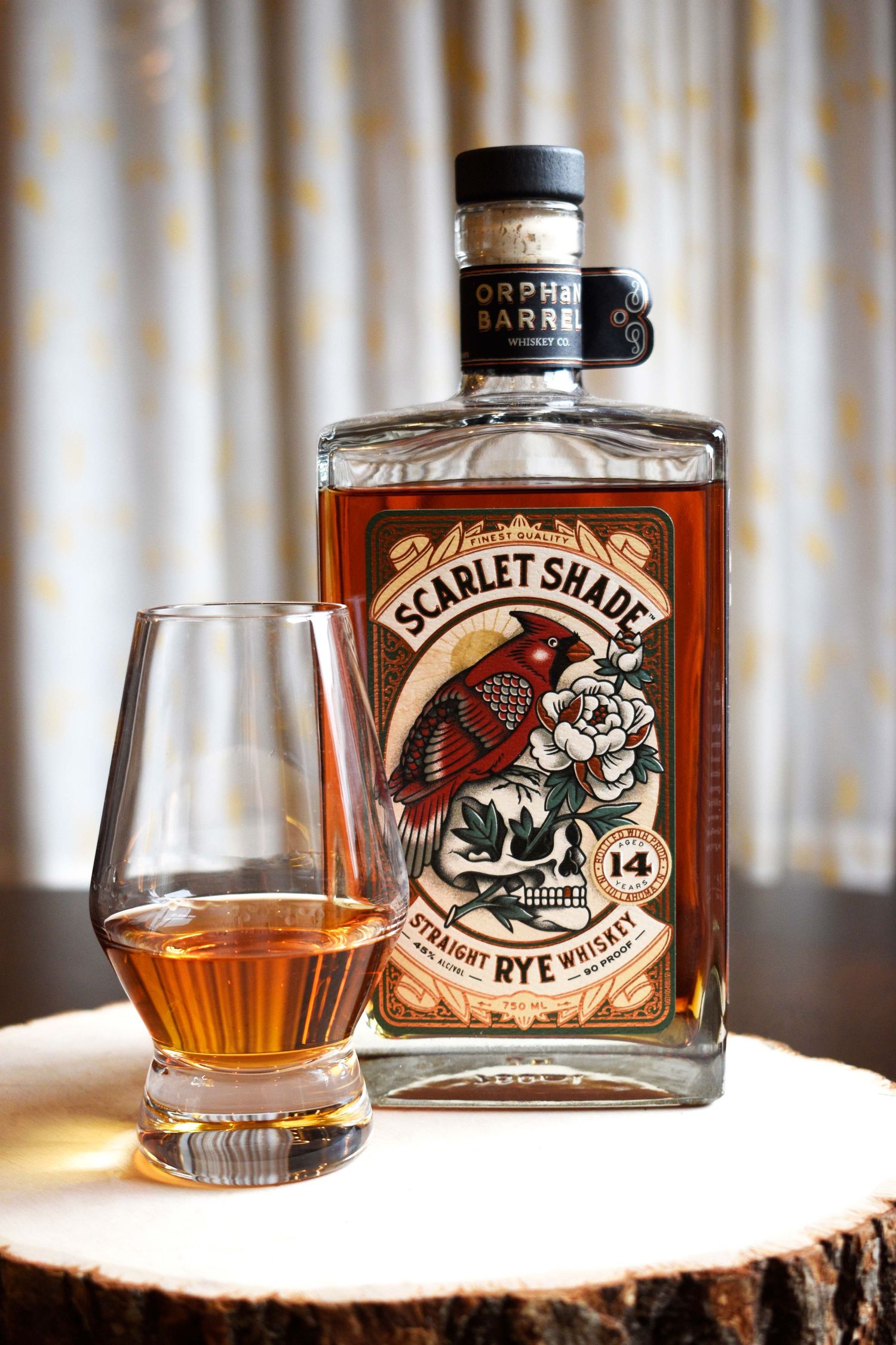 Orphan Barrel Scarlet Shade 14-year straight rye whiskey bottle beside a filled Glencairn glass on a wood slab.