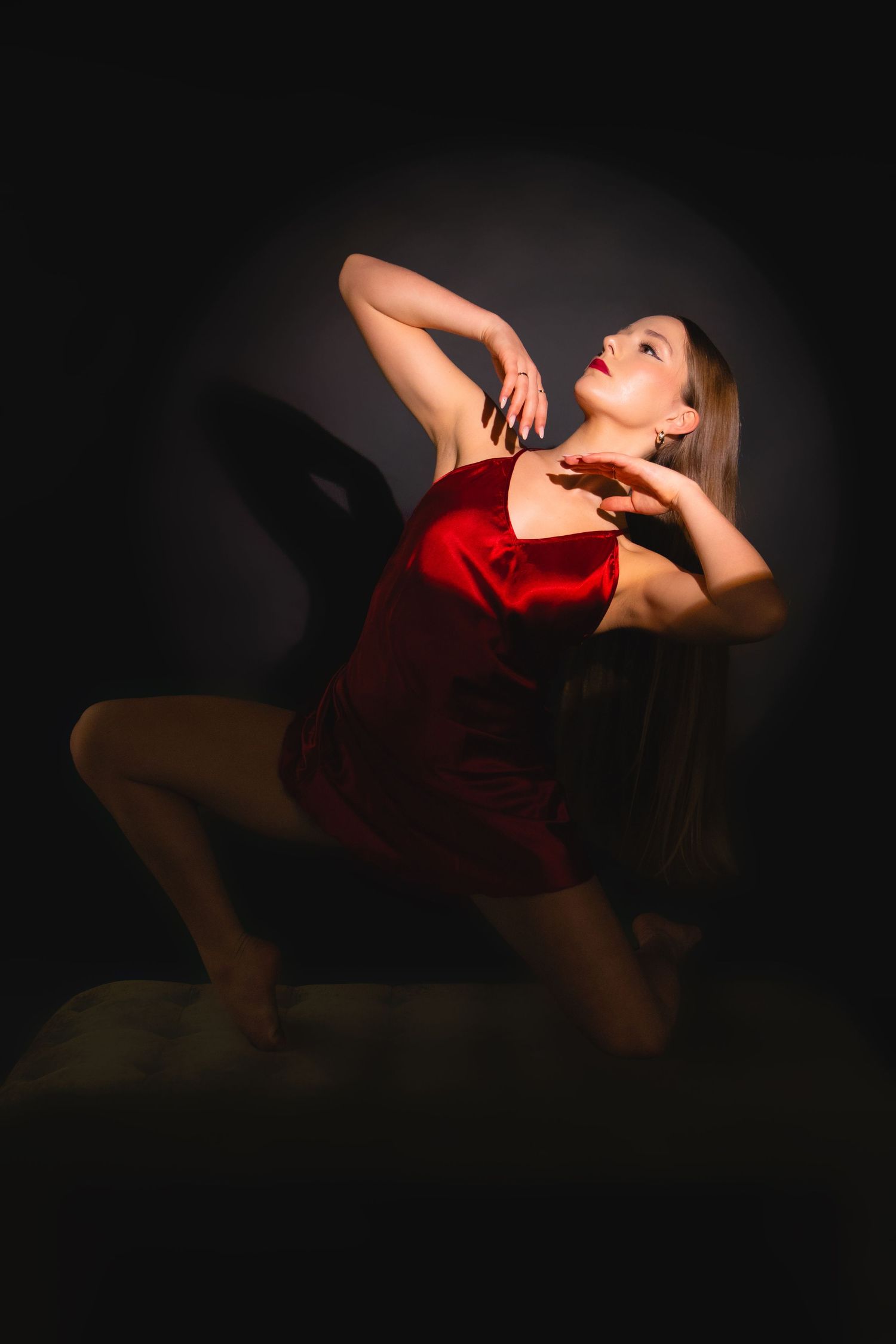 A dancer in a red satin dress poses dramatically against a dark background with spotlight illumination.