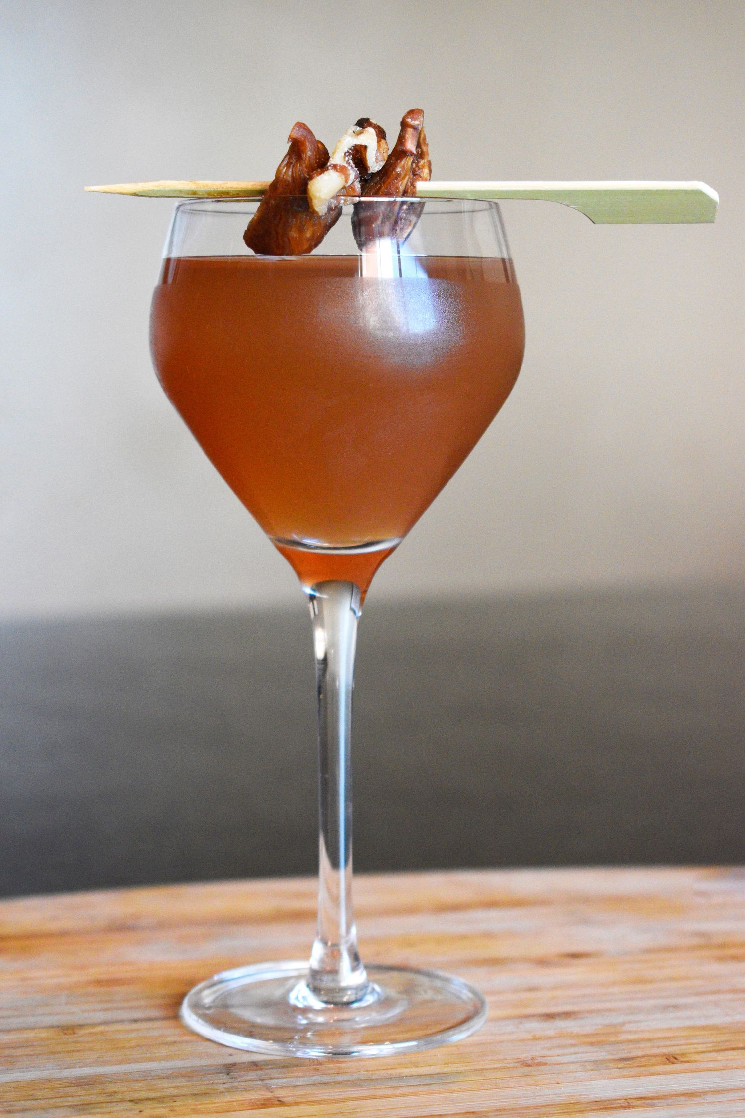 Pink cocktail served in martini glass garnished with dried mushrooms on a bamboo skewer.