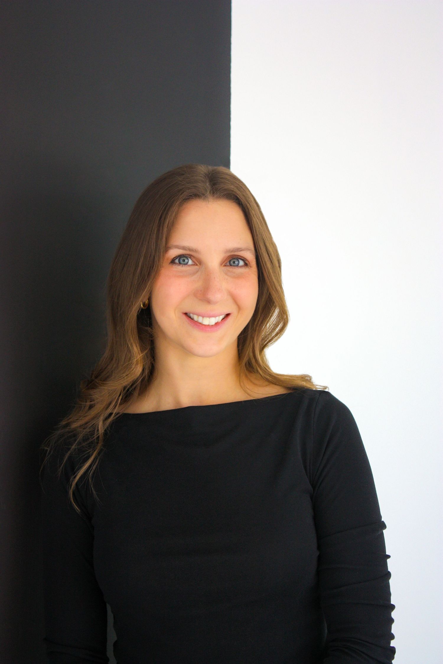 Smiling young woman with long brown hair wearing a black top, posed against a black and white background. Branding photography Tampa, FL.