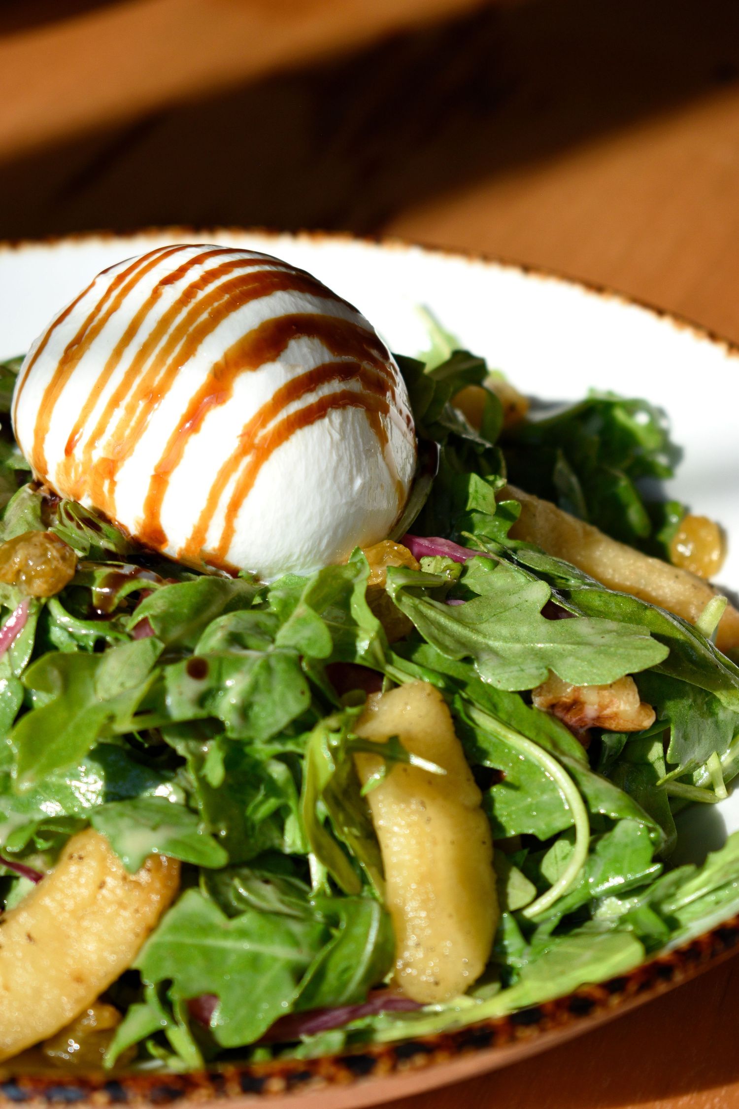 Fresh arugula salad with burrata cheese drizzled with balsamic glaze and caramelized pears.