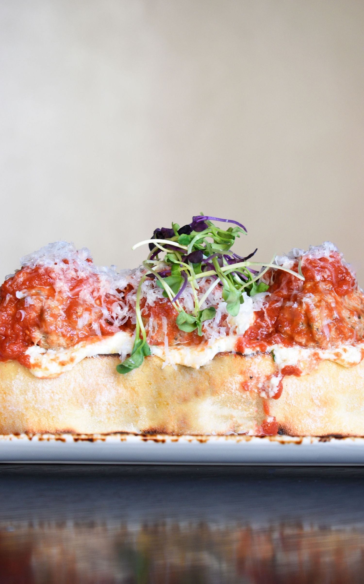 A meatball sub sandwich topped with tomato sauce, melted cheese, and fresh microgreens on a white plate.