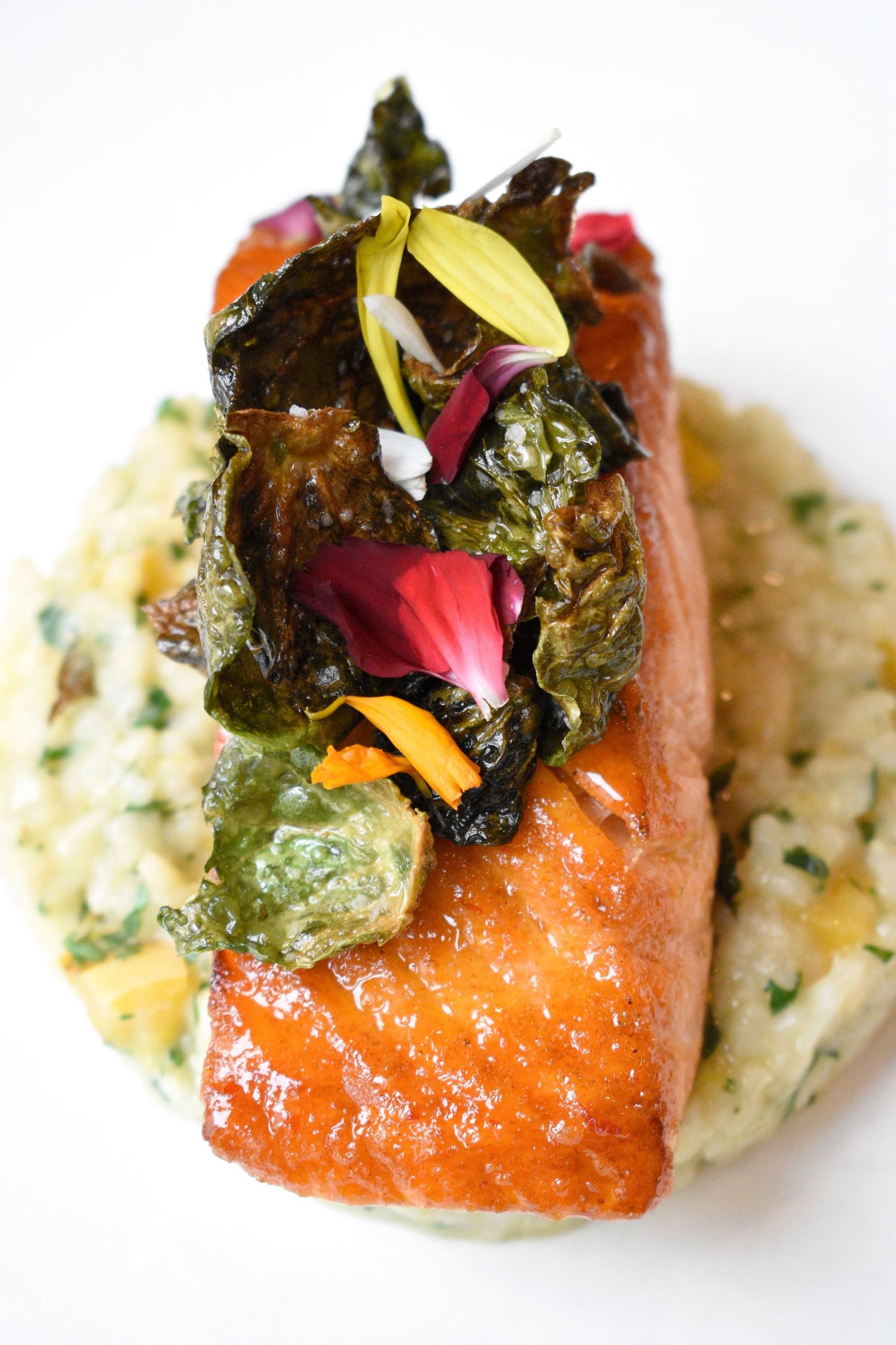 Seared salmon fillet topped with crispy kale and edible flowers served over herbed risotto.