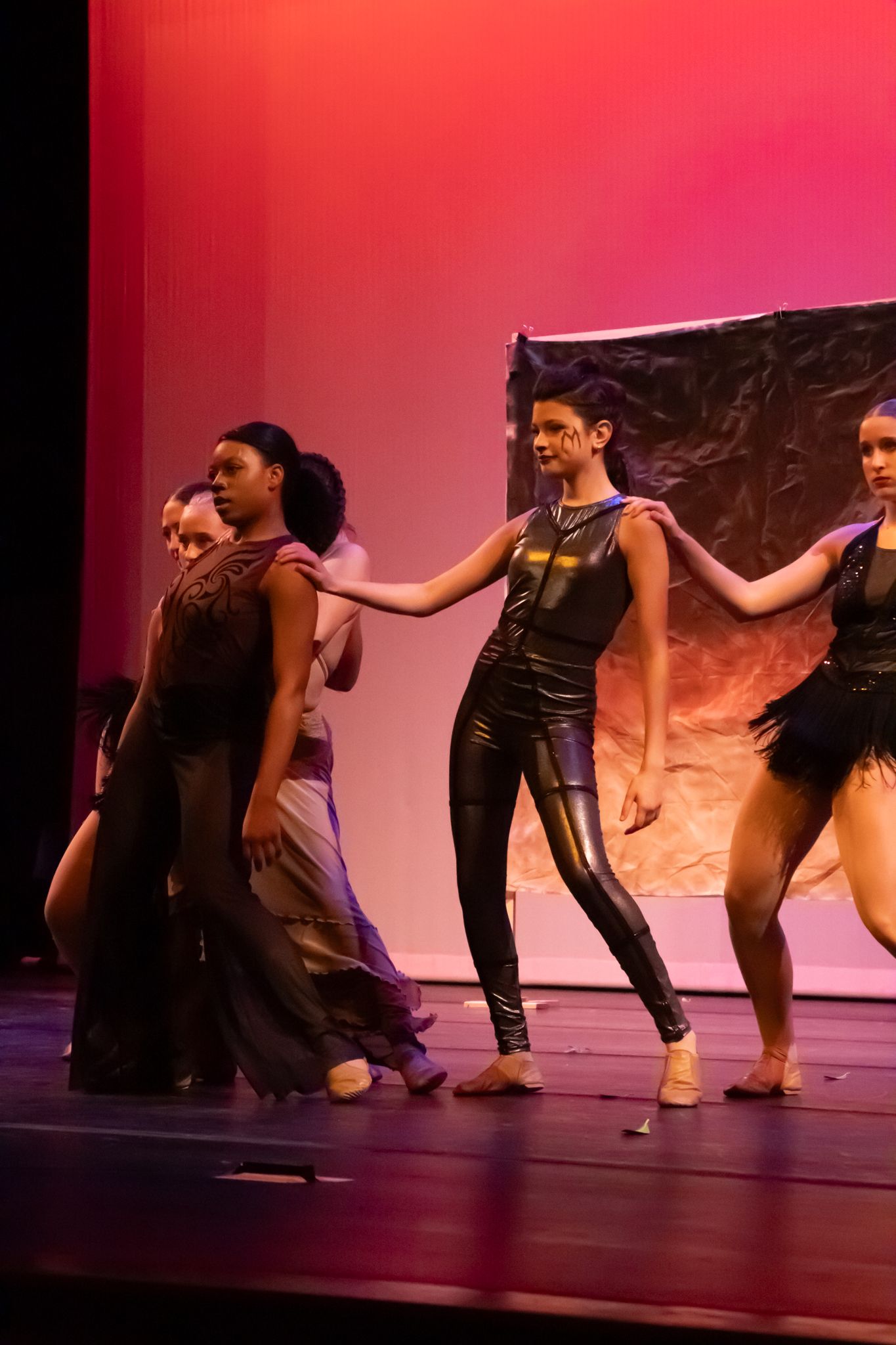 Dancers perform on stage in dramatic black costumes under red lighting during a contemporary dance recital.
