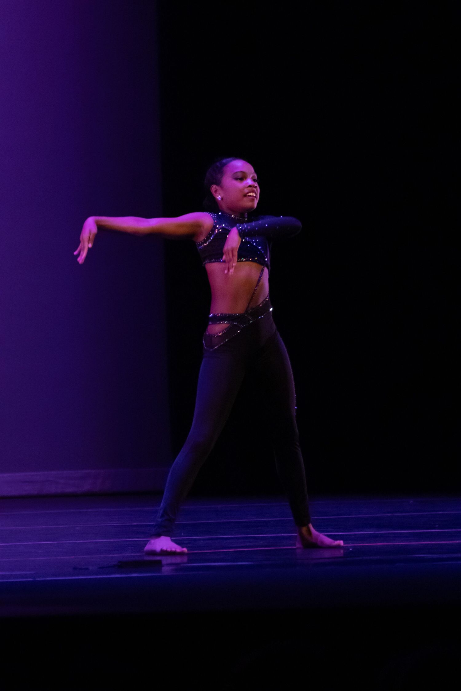 A young female dancer in a blue sequined crop top and black pants performs an expressive contemporary dance solo.
