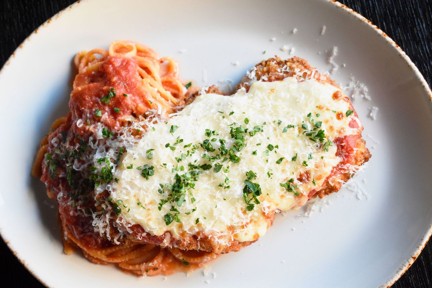 Classic chicken parmesan with melted mozzarella, tomato sauce, and parmesan over spaghetti on white plate.