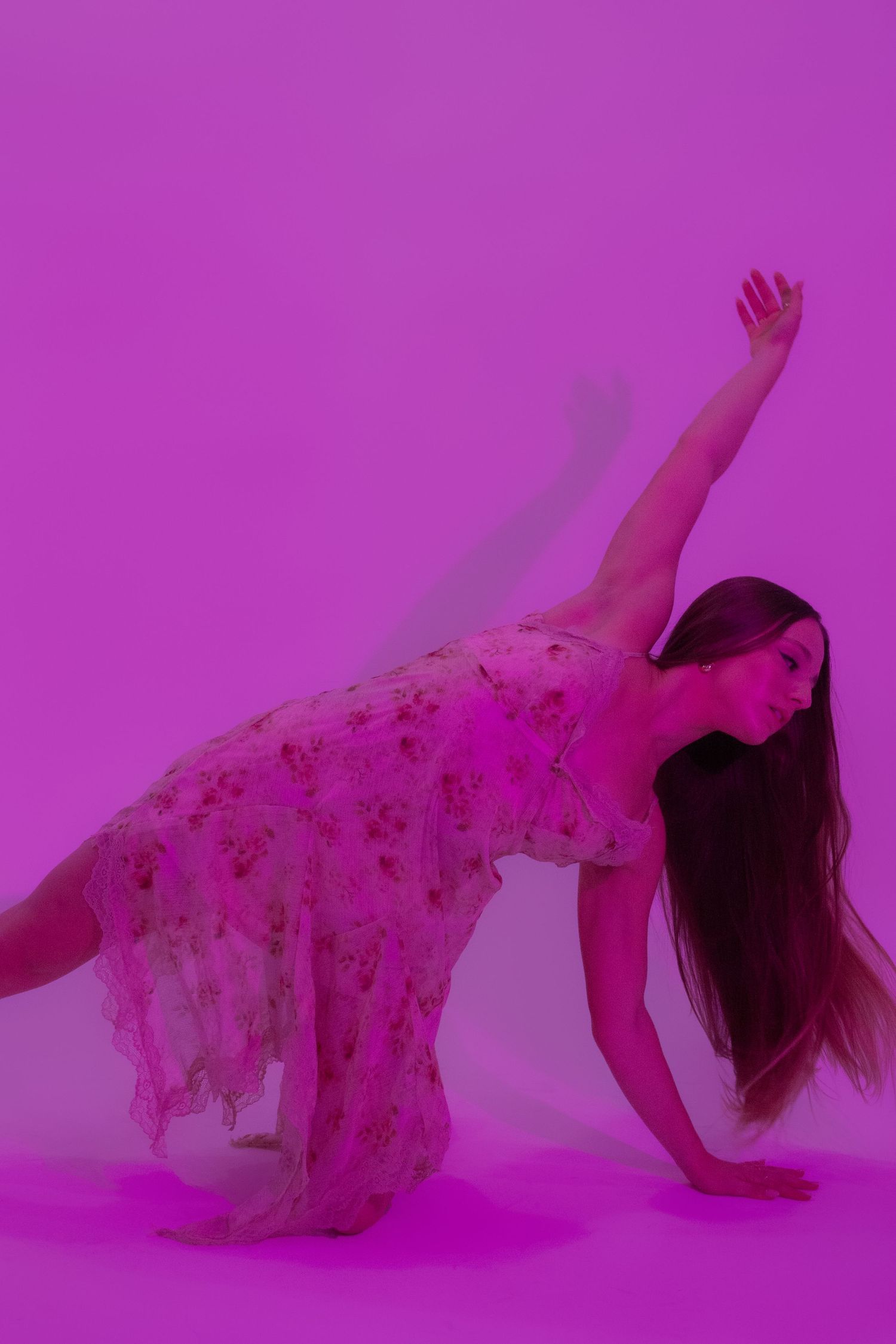 Woman in floral dress striking a dramatic dance pose against a vibrant pink-purple studio background.