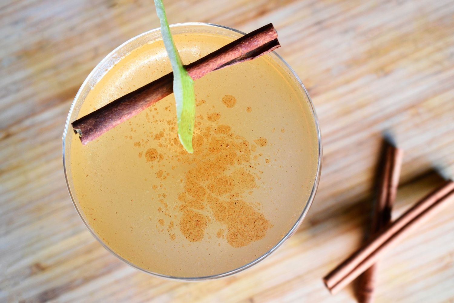 Overhead view of a creamy spiced cocktail garnished with cinnamon sticks and a green straw.