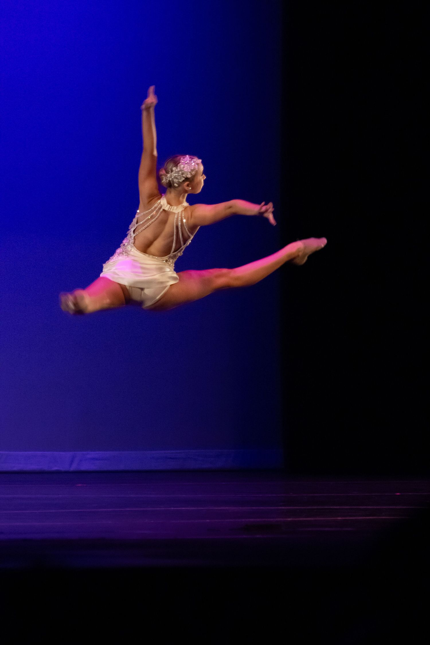 A skilled dancer leaps mid-air in a graceful split jump on a blue-lit performance stage.